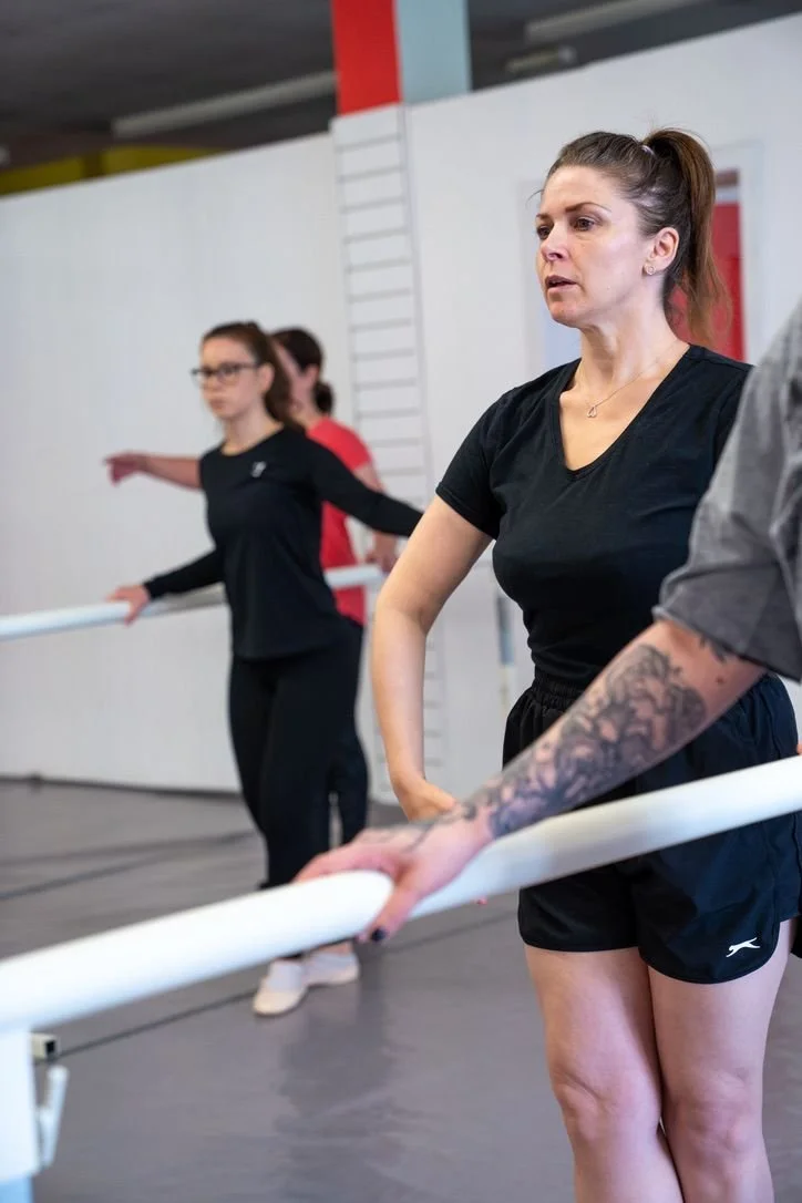 Adult ballet dancers practising at the barre during a group class.