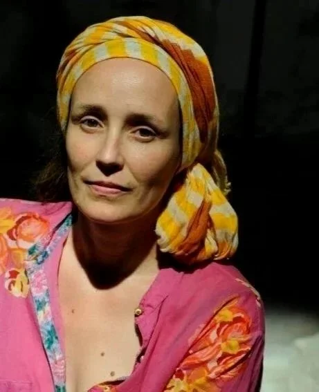 A woman wearing a colorful headscarf and a pink blouse with floral accents