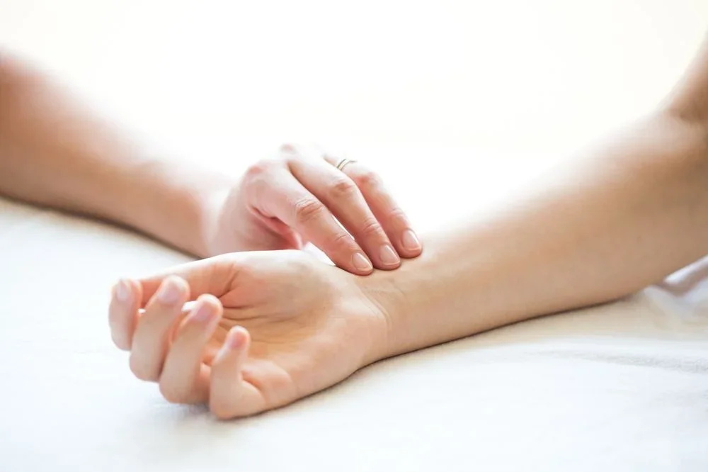 A person receiving a wrist massage on their left arm, with hands gently pressing on the wrist and forearm.