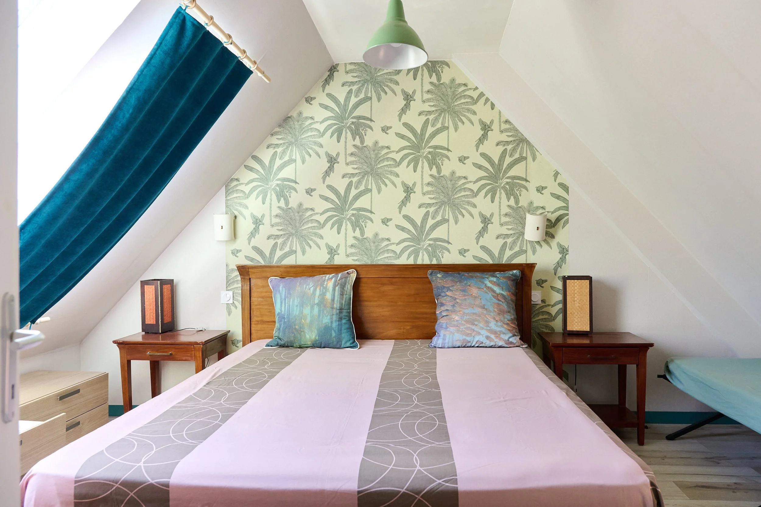Bedroom with a sloped ceiling, featuring a bed with two pillows and window with turquoise curtains.