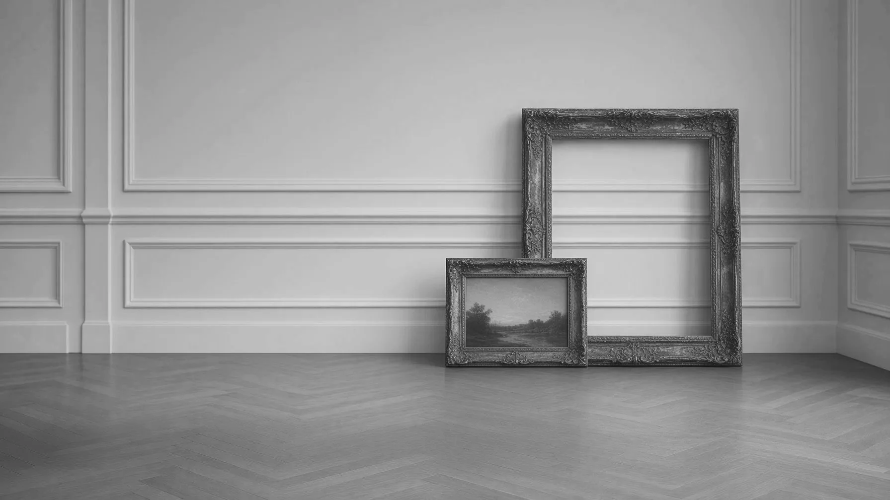 A black and white photo of two empty ornate picture frames leaning against a white paneled wall in an empty room with wooden flooring.