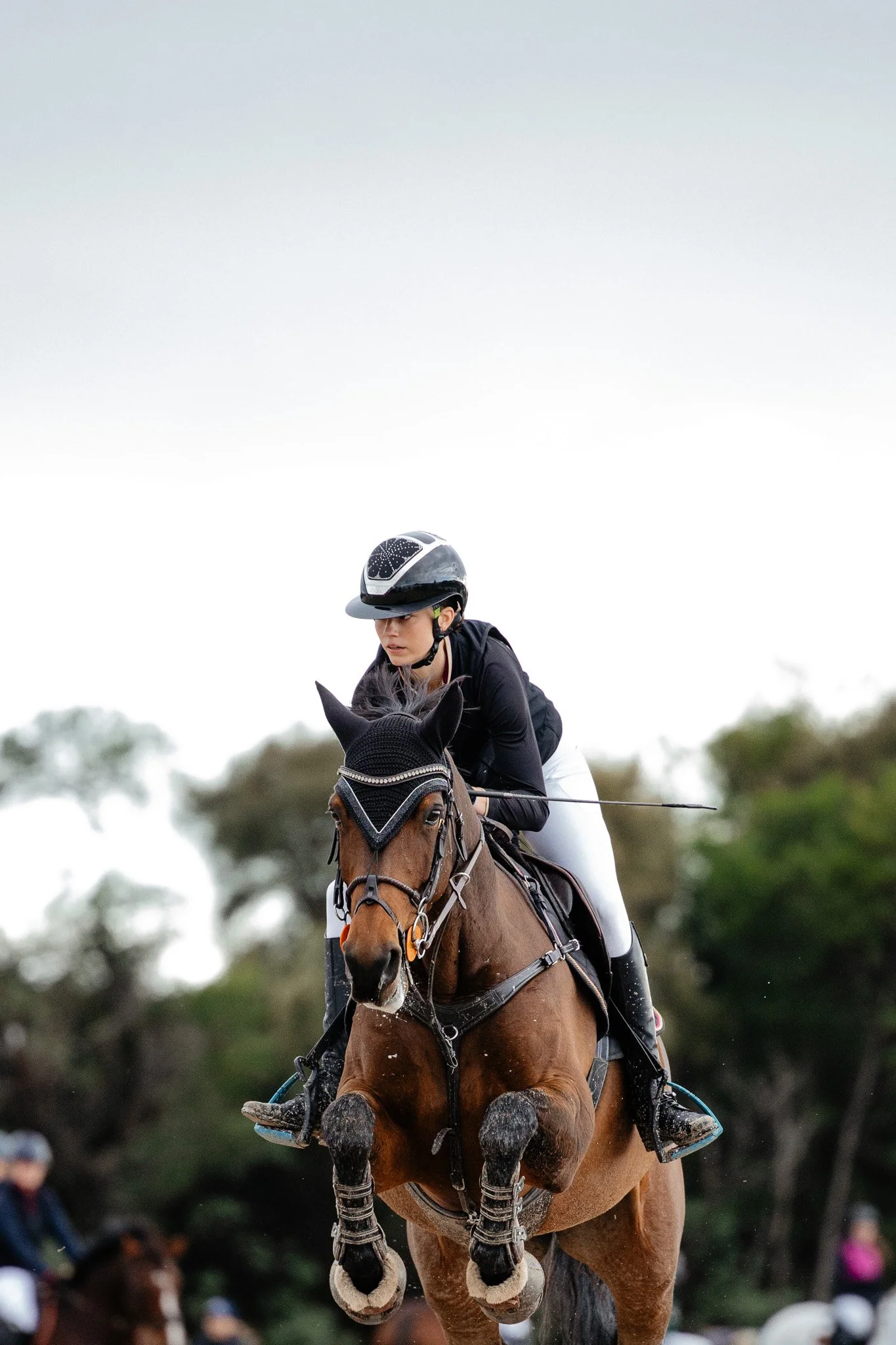 A female equestrian riding a galloping horse during a show jumping event.