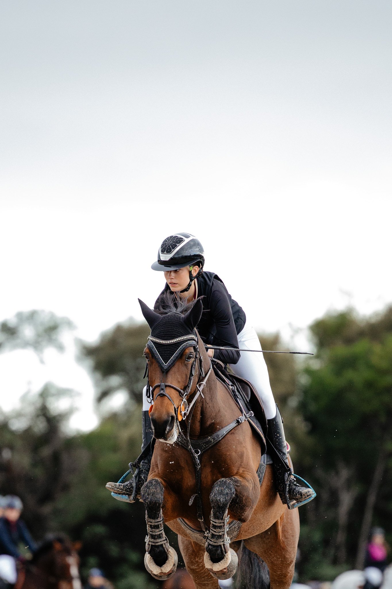 A female equestrian rider with a black helmet riding a brown horse during a competition.