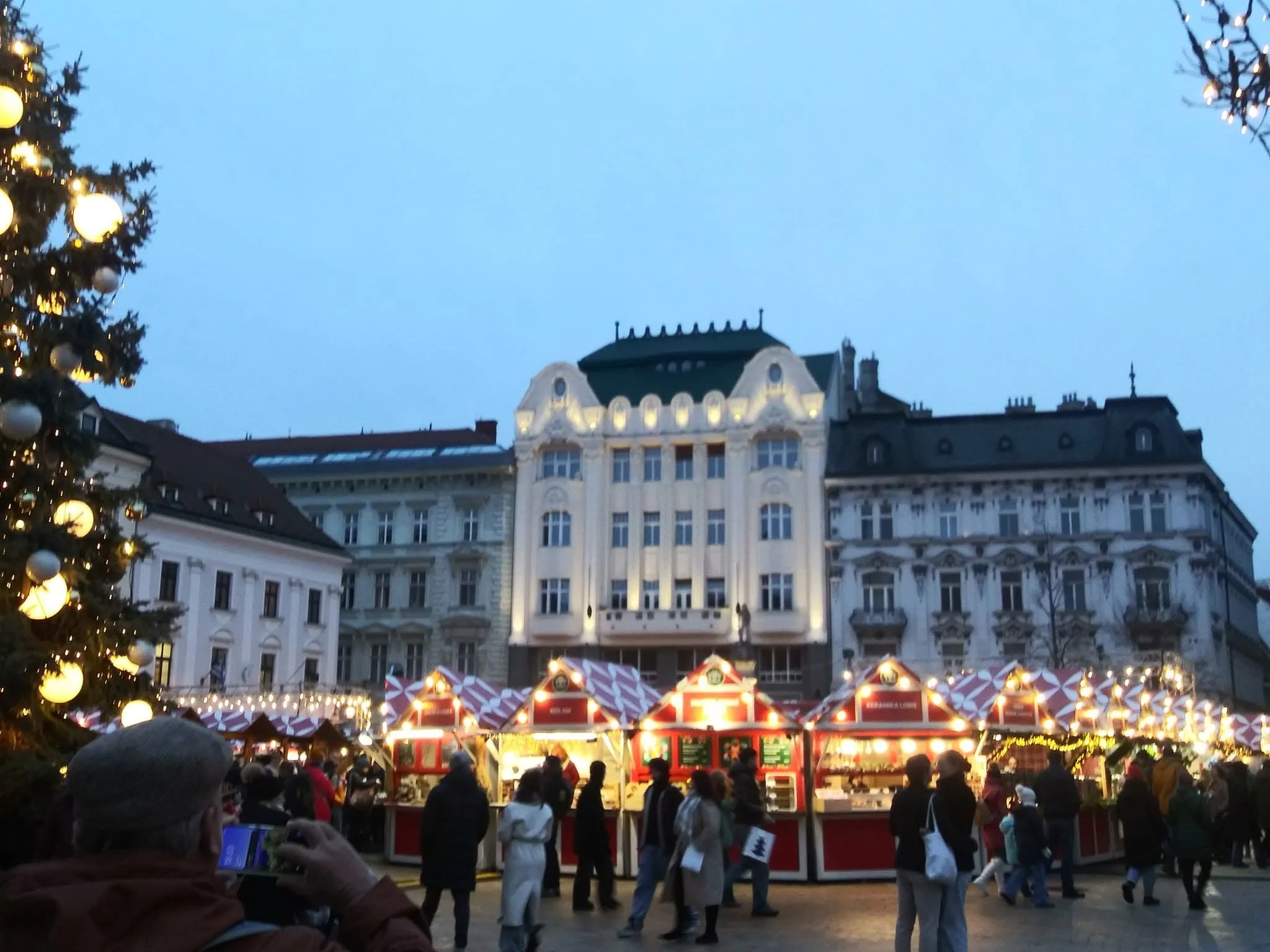 Travelers visiting a brightly lit European Christmas market during the holiday season.