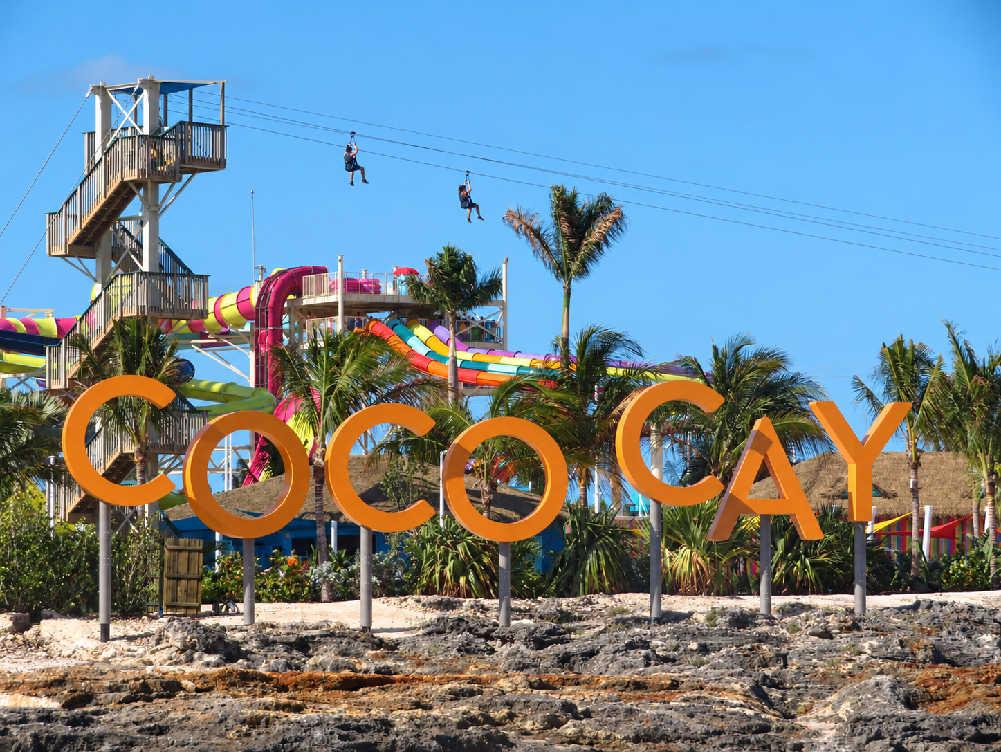 CocoCay entrance sign beneath zip-line riders and colorful waterslides during a 2019 Royal Caribbean cruise.