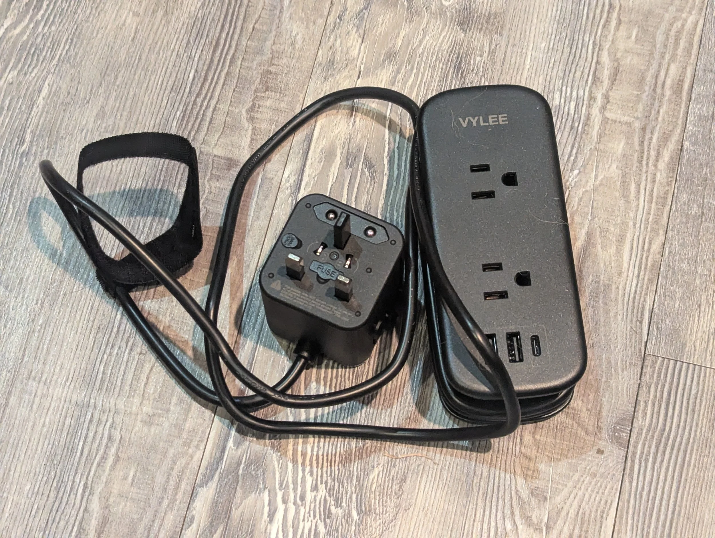 VYLEE universal travel power strip with two AC outlets, USB charging ports and built-in UK travel plug.