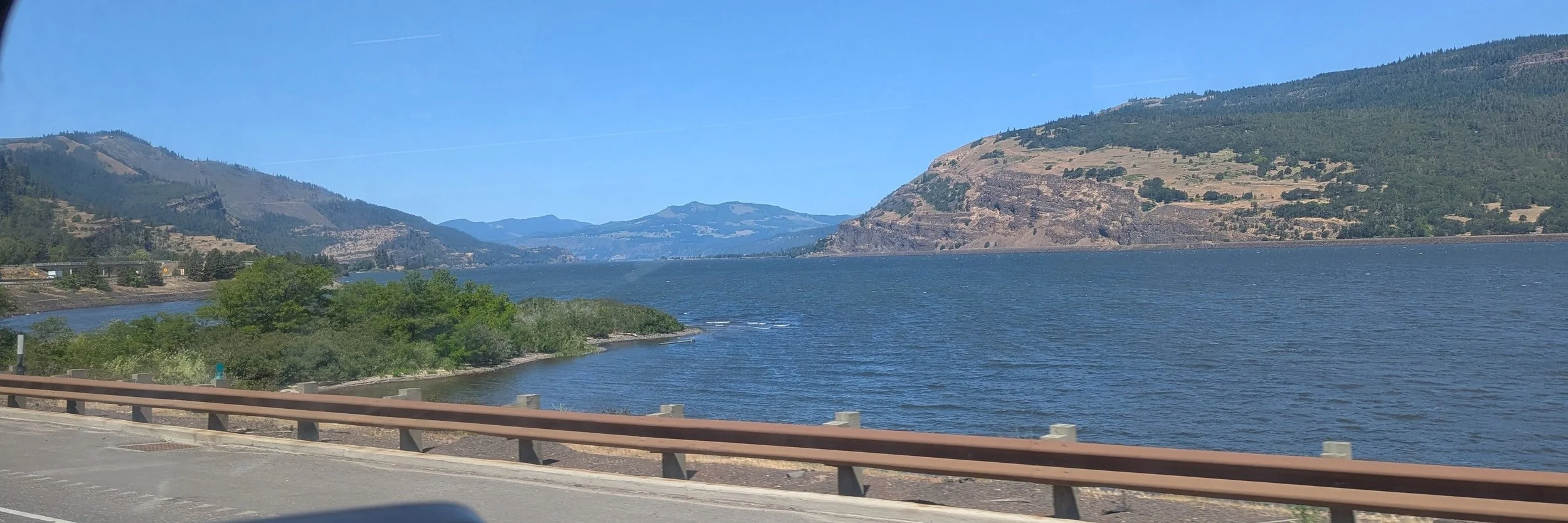 Scenic road winding past a towering basalt cliff and dry hills in Oregon's Columbia River Gorge.
