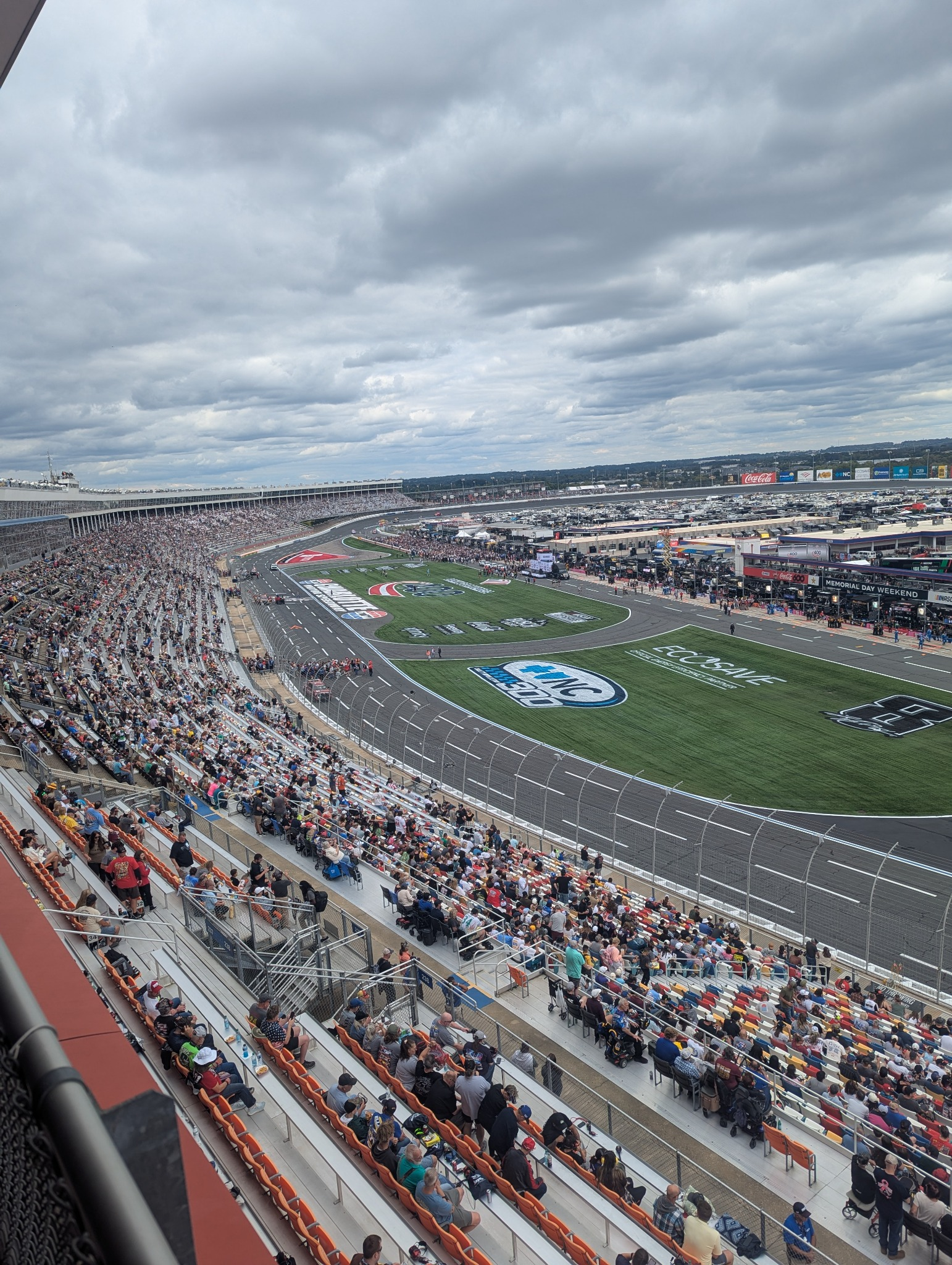 Wide-angle Google Pixel 7 photograph of Charlotte Motor Speedway showing the grandstands, pit road, racing surface, and dramatic cloud cover.