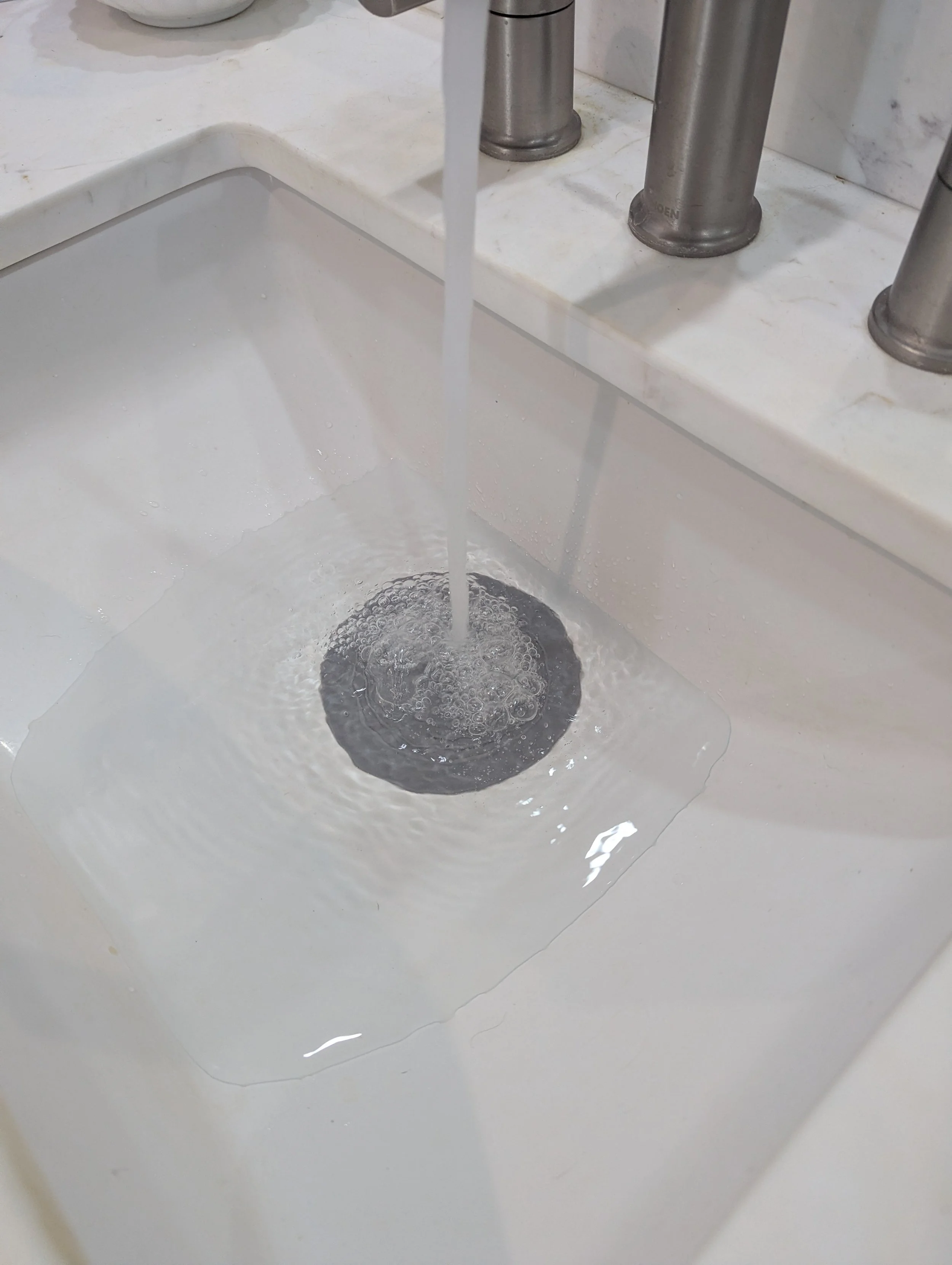 Flat silicone drain stopper sealing a bathroom sink so it can be filled for hand washing clothes while traveling.