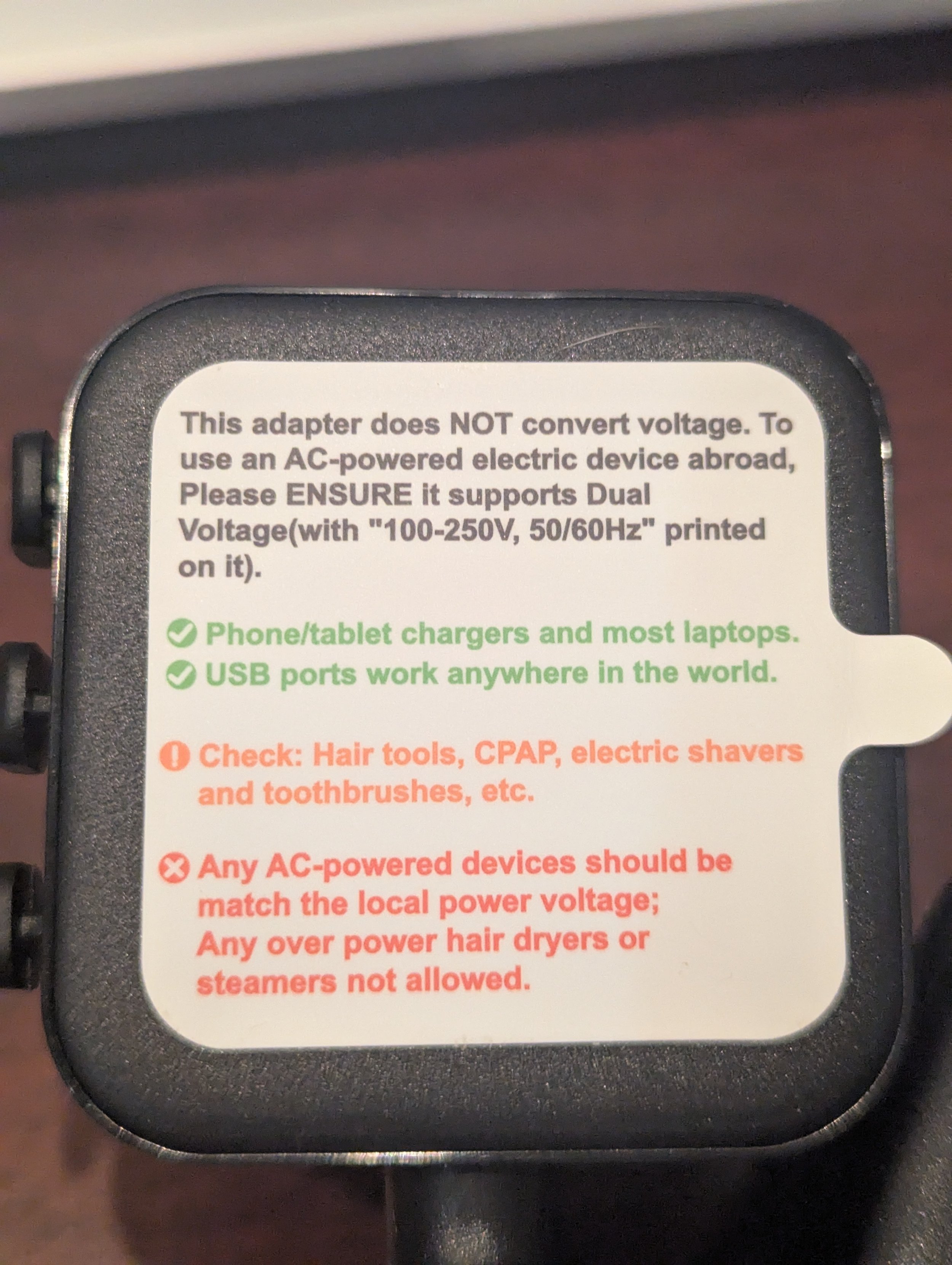 Warning label on an international travel power strip explaining that the adapter does not convert voltage and connected devices must support local voltage.
