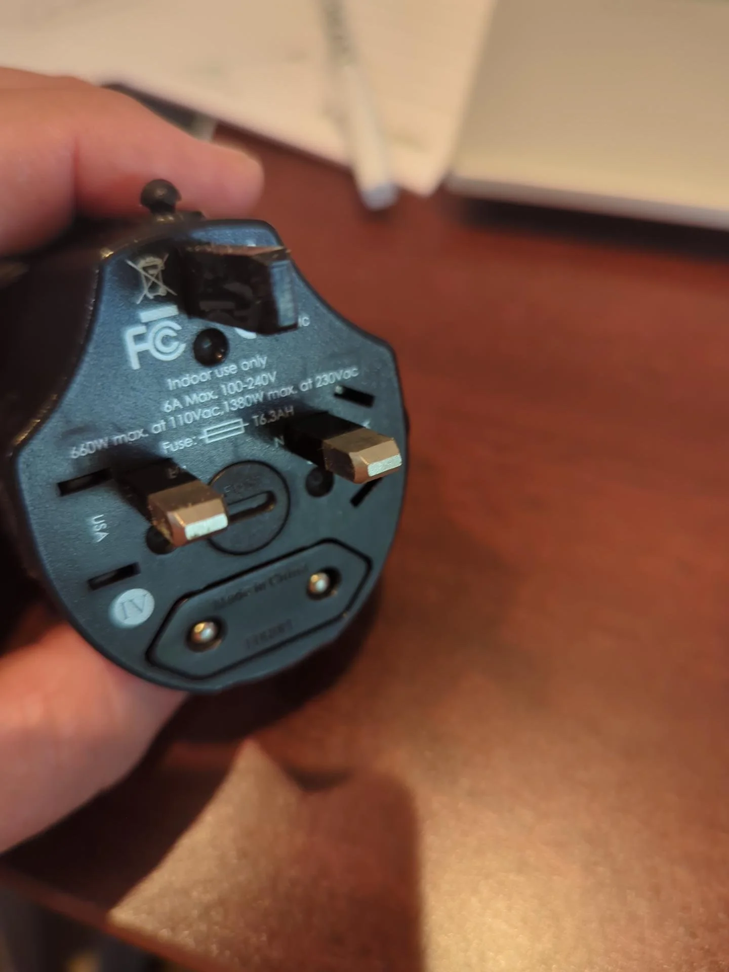 Compact universal travel adapter shown with different international plug configurations, carried as a backup to an international travel power strip.