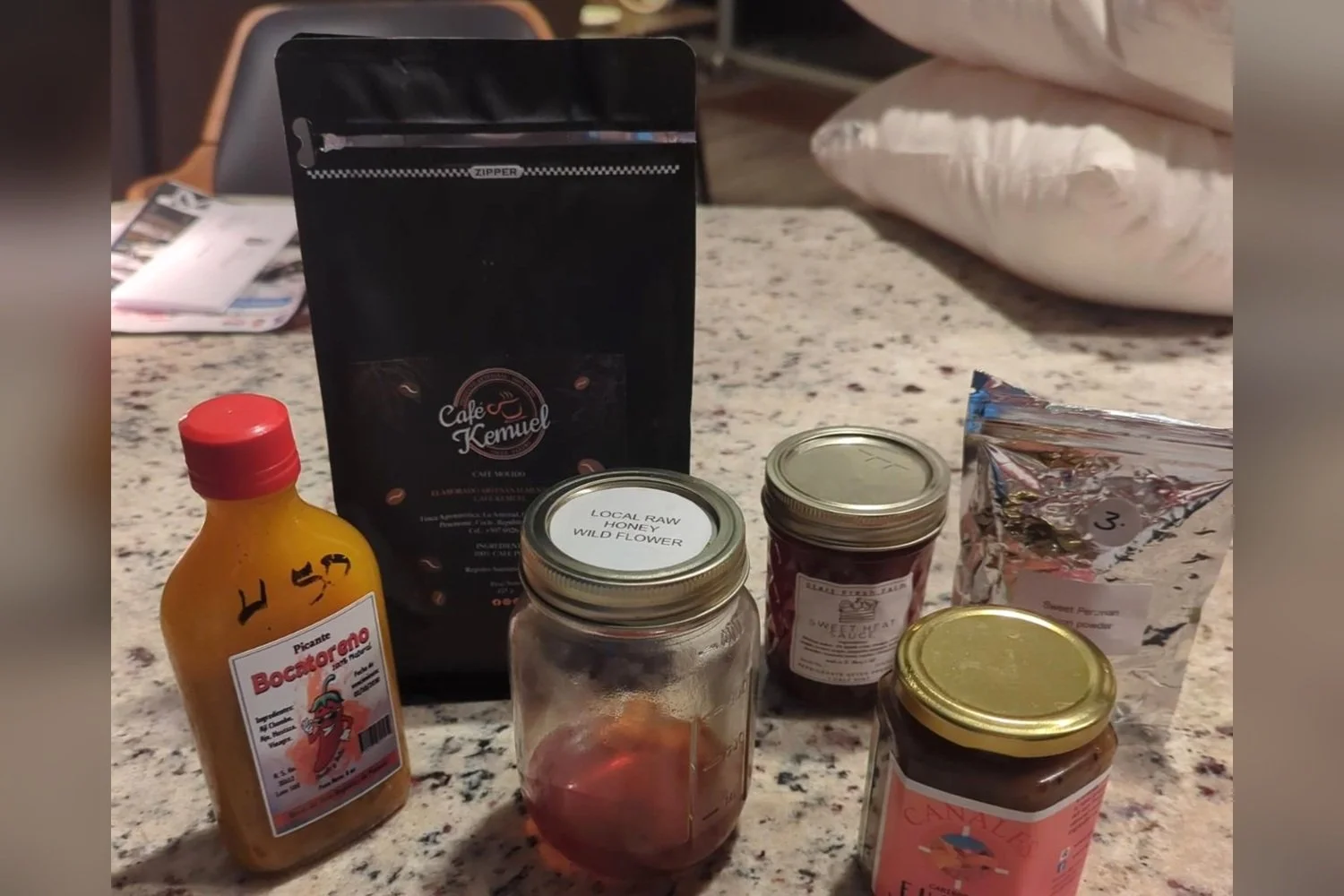 Collection of farmers market souvenirs arranged on a kitchen countertop, including jars of local honey, specialty coffee, hot sauces, and seasonings.