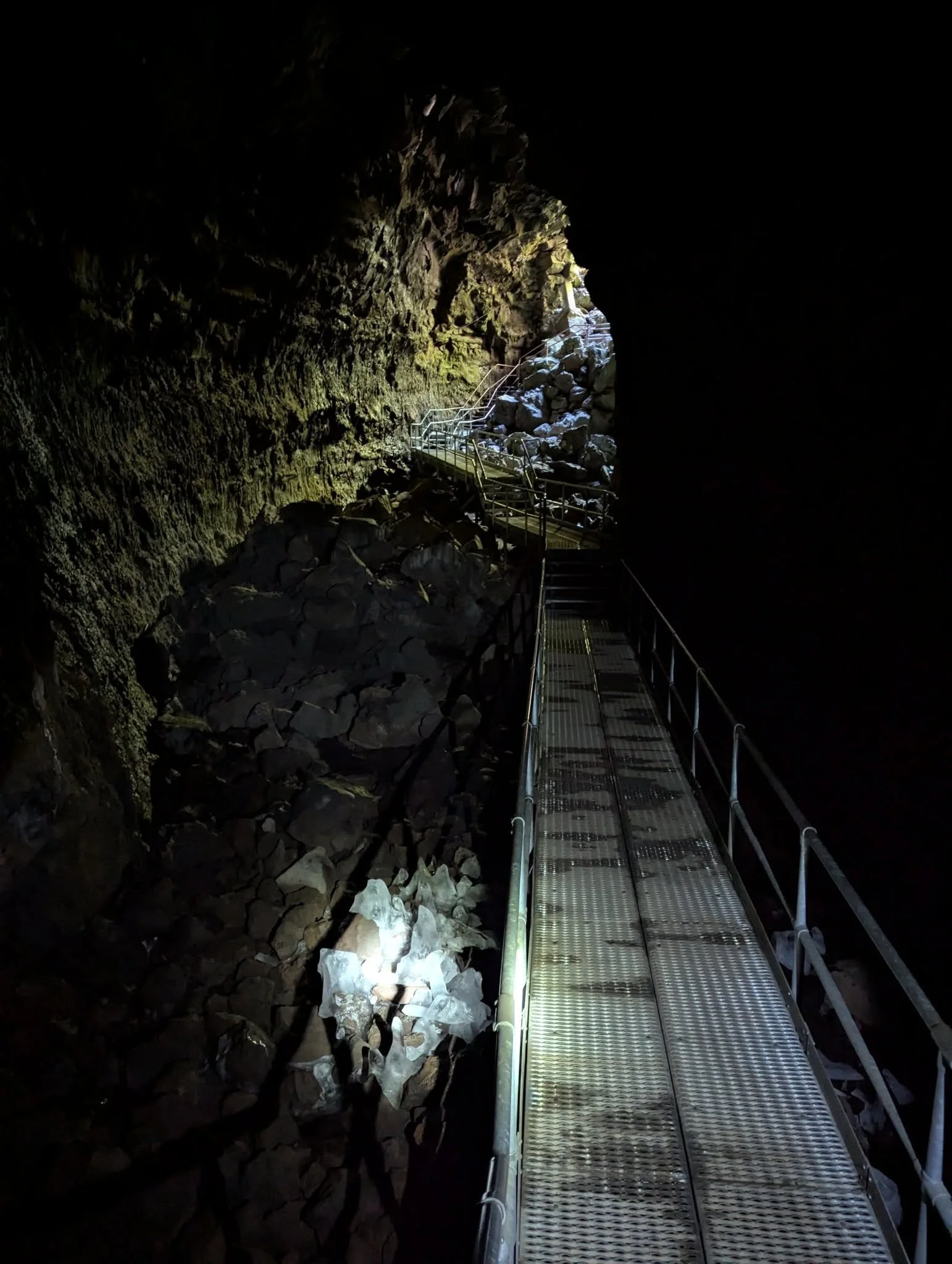 Metal walkway with handrails crossing uneven volcanic rock inside the dark Lava River Cave in Central Oregon.