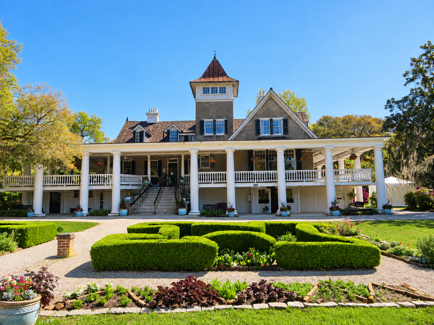 Historic Southern house with a wide columned porch and landscaped gardens beneath a clear blue sky.