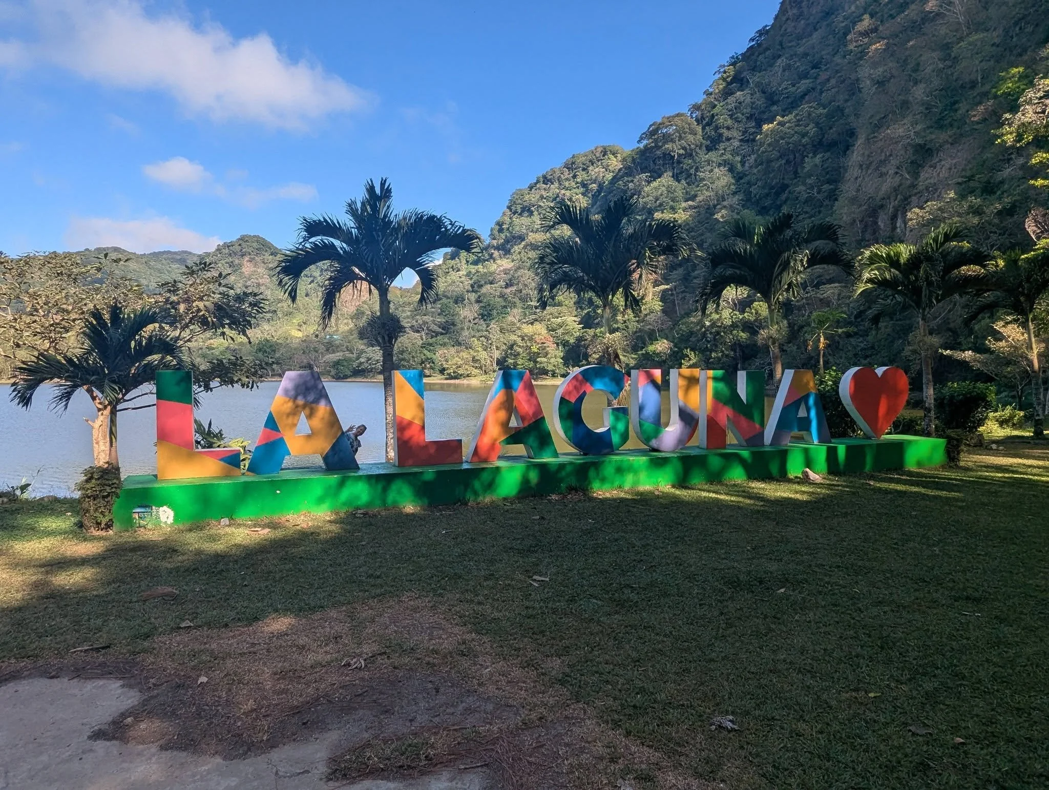 Colorful La Laguna sign beside a peaceful mountain lake surrounded by palm trees and lush forest in Panama.