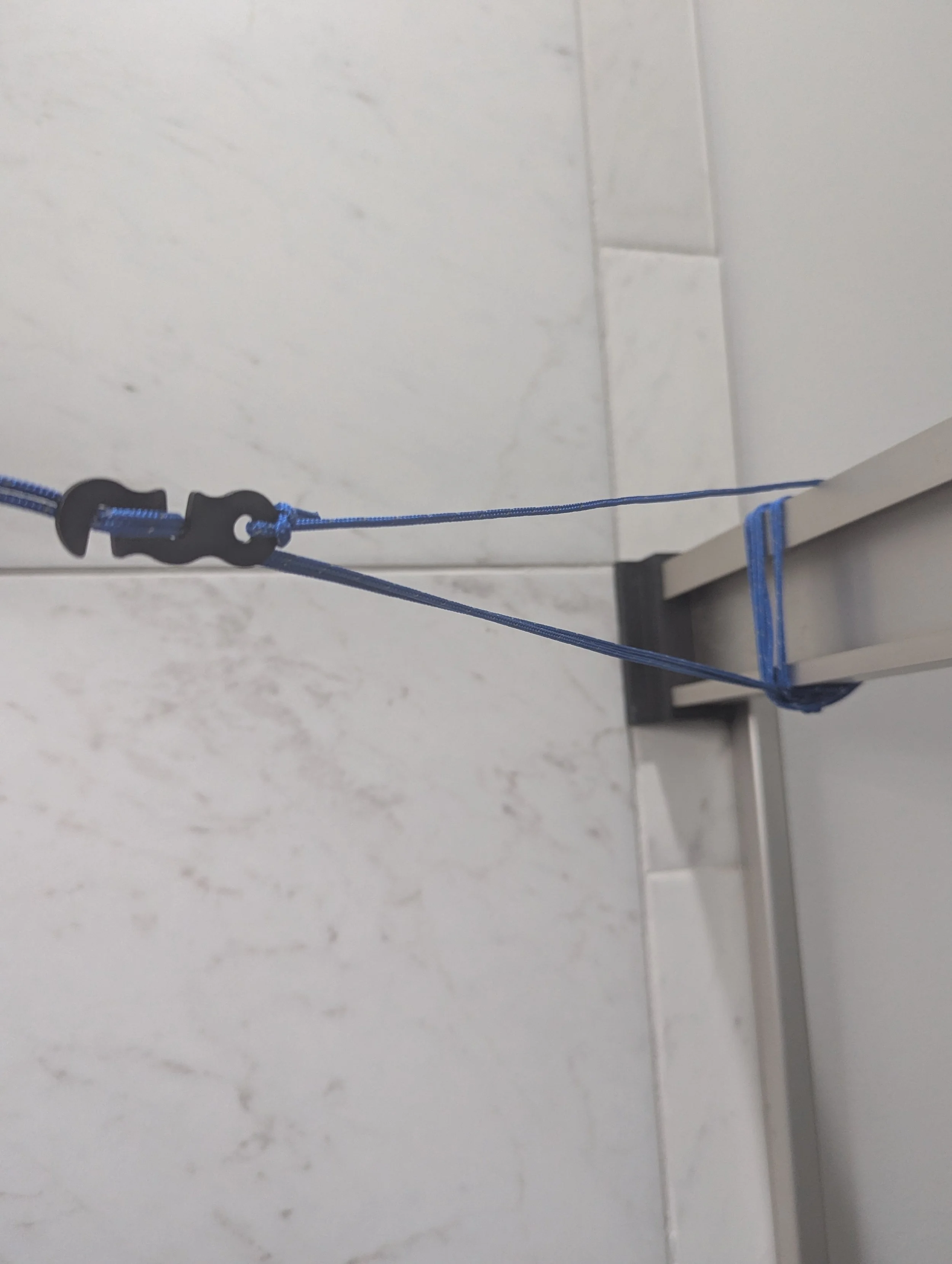 Portable travel clothesline wrapped securely around a fixed shower-door rail.