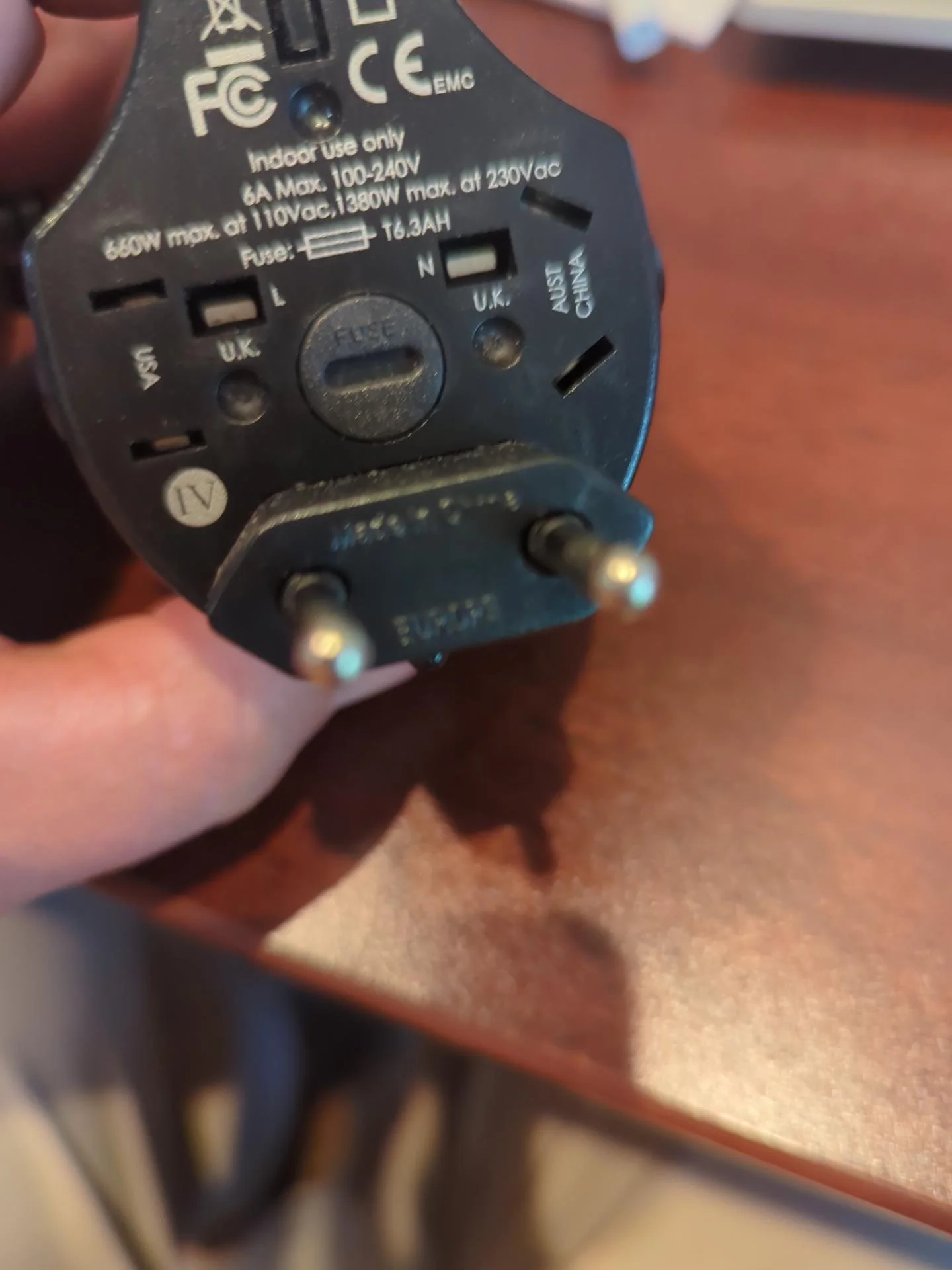 Compact universal travel adapter shown with different international plug configurations, carried as a backup to an international travel power strip.