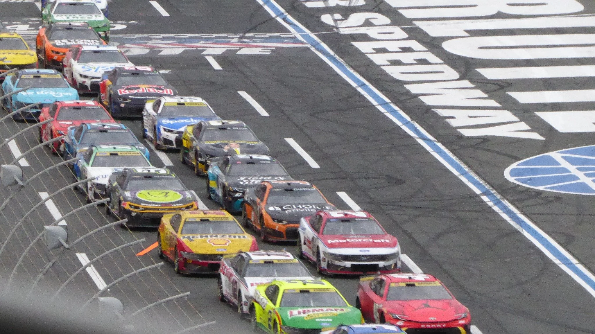 Telephoto photograph from the Panasonic Lumix ZS50 showing a tightly packed field of NASCAR Cup Series cars at Charlotte Motor Speedway.