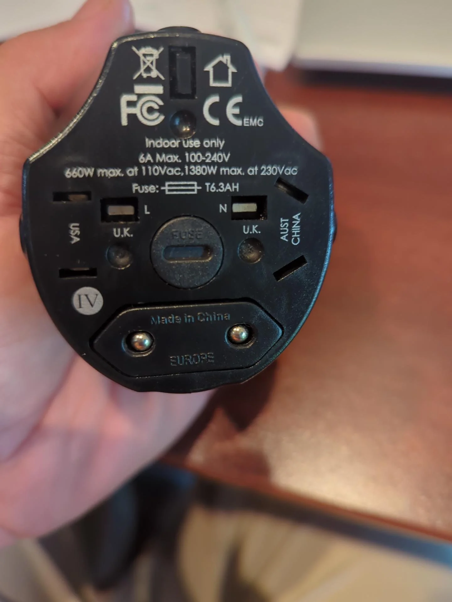 Compact universal travel adapter shown with different international plug configurations, carried as a backup to an international travel power strip.