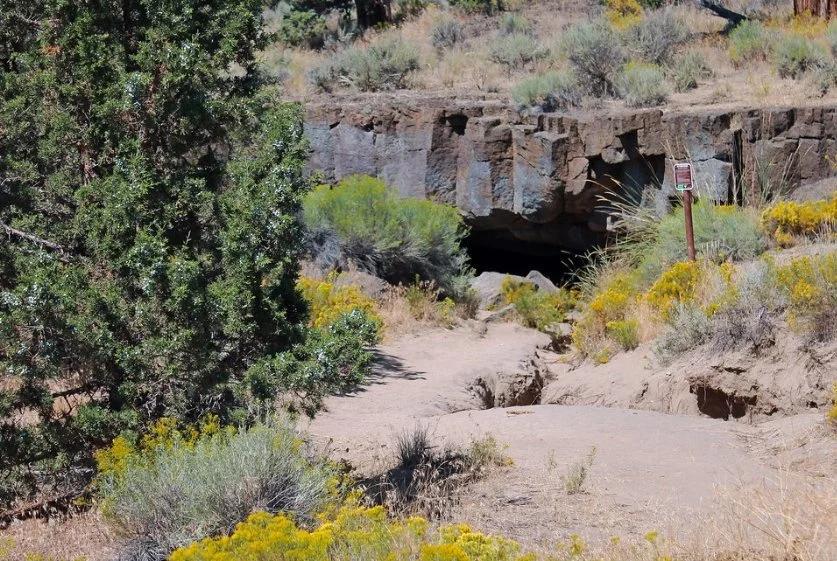 Natural lava-rock entrance and dirt walking path at Redmond Caves Recreation Site near Redmond, Oregon.