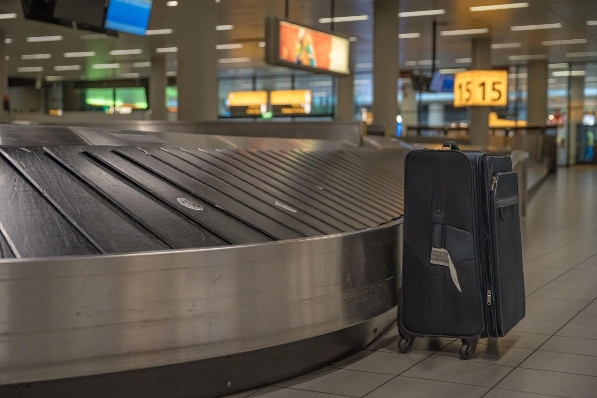 Suitcase beside an empty airport baggage carousel representing delayed luggage.