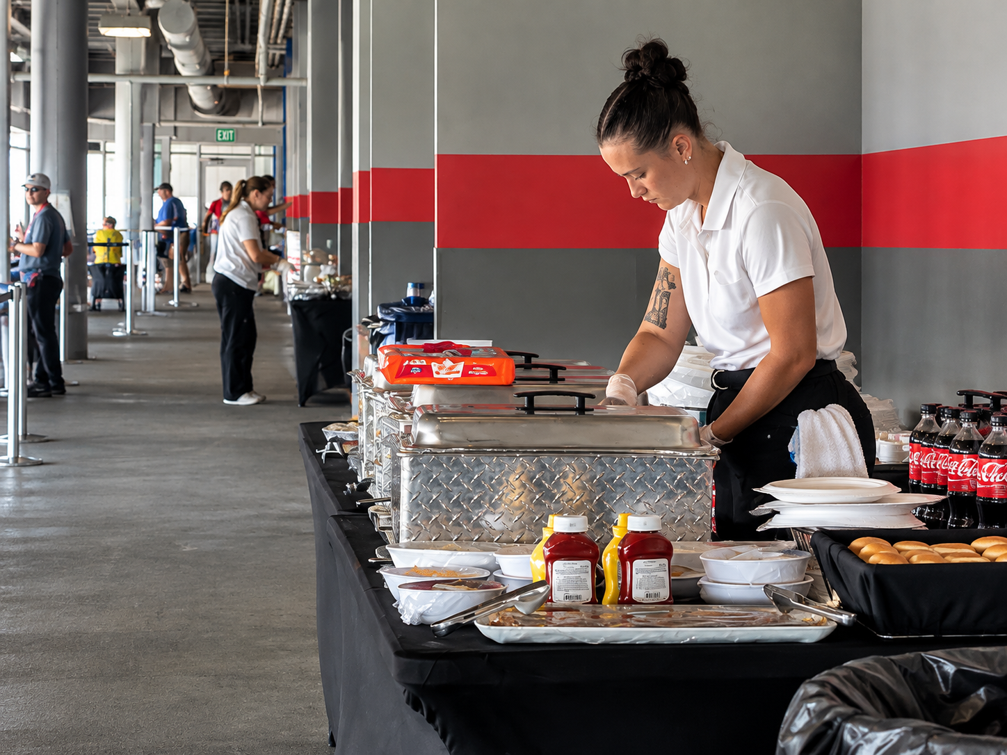 Food service staff preparing the buffet at Charlotte Motor Speedway, with covered serving trays, condiments, beverages, and dining supplies.