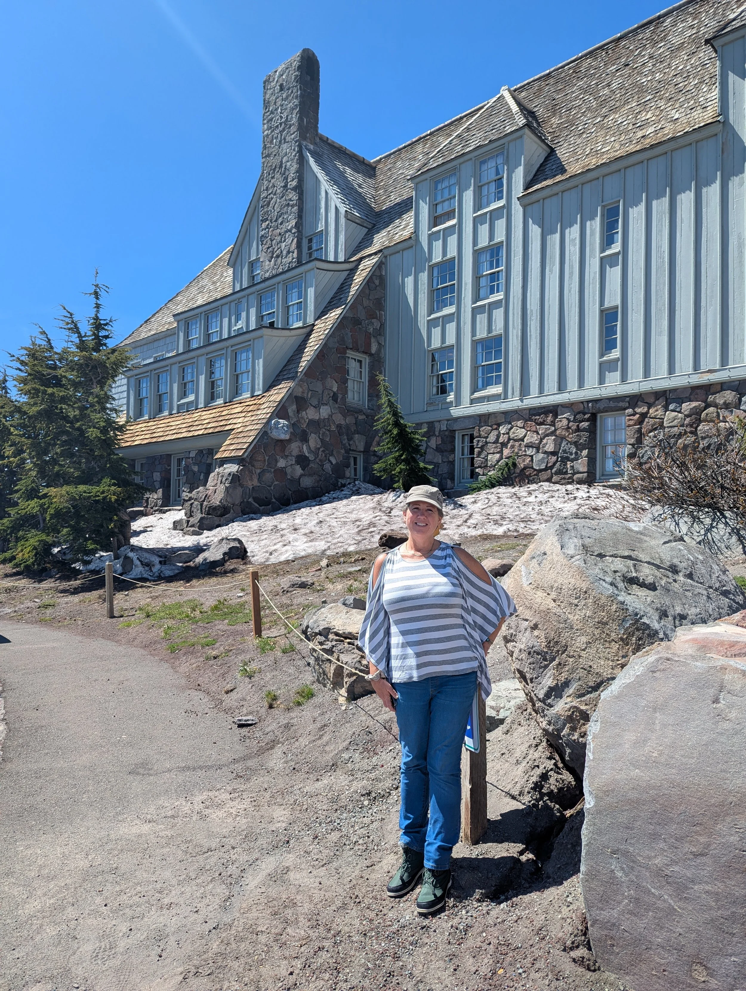 Gina standing outside historic Timberline Lodge on Mount Hood, Oregon, with rustic stone architecture and lingering spring snow.