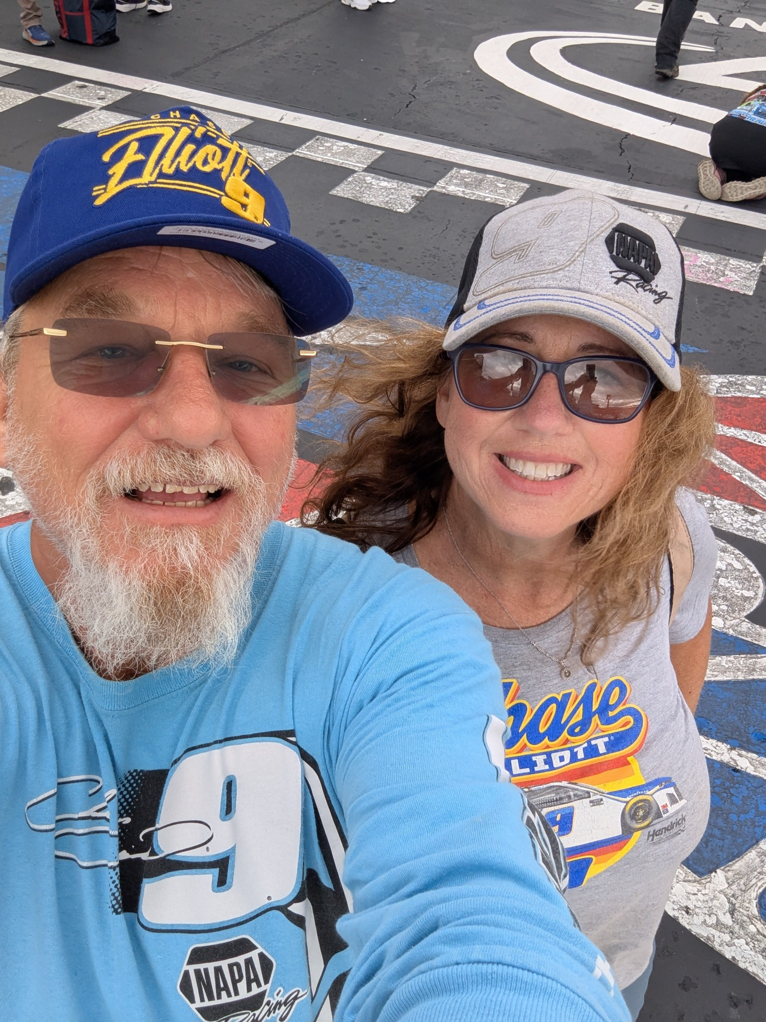 Two NASCAR fans taking a selfie on the racing surface at Charlotte Motor Speedway during the pre-race Track Pass experience.