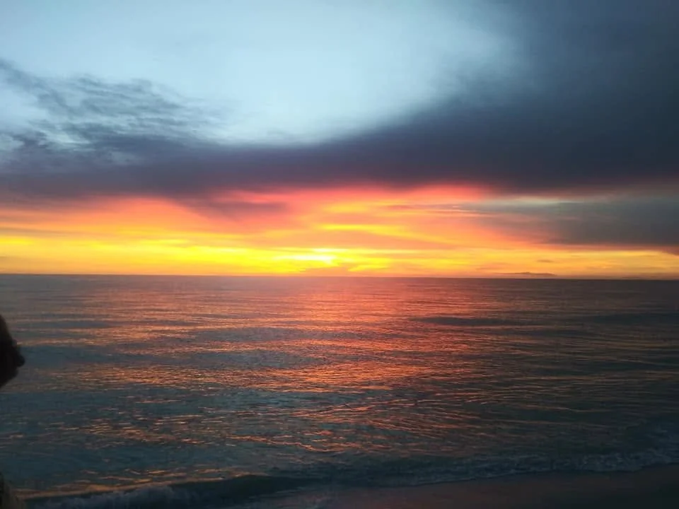 Orange and gold sunset reflecting across the Gulf of Mexico at Boca Grande, Florida, beneath dark evening clouds.