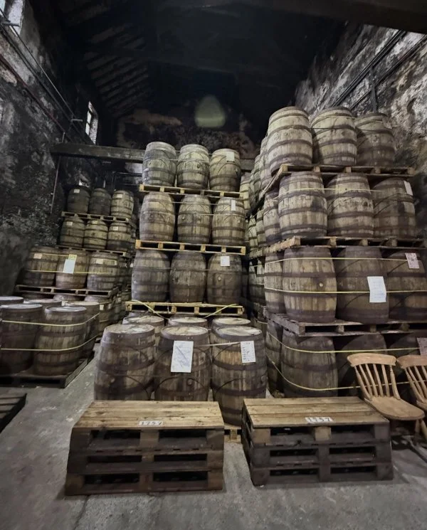 Rows of wooden whiskey barrels aging inside the historic Kilbeggan Distillery.