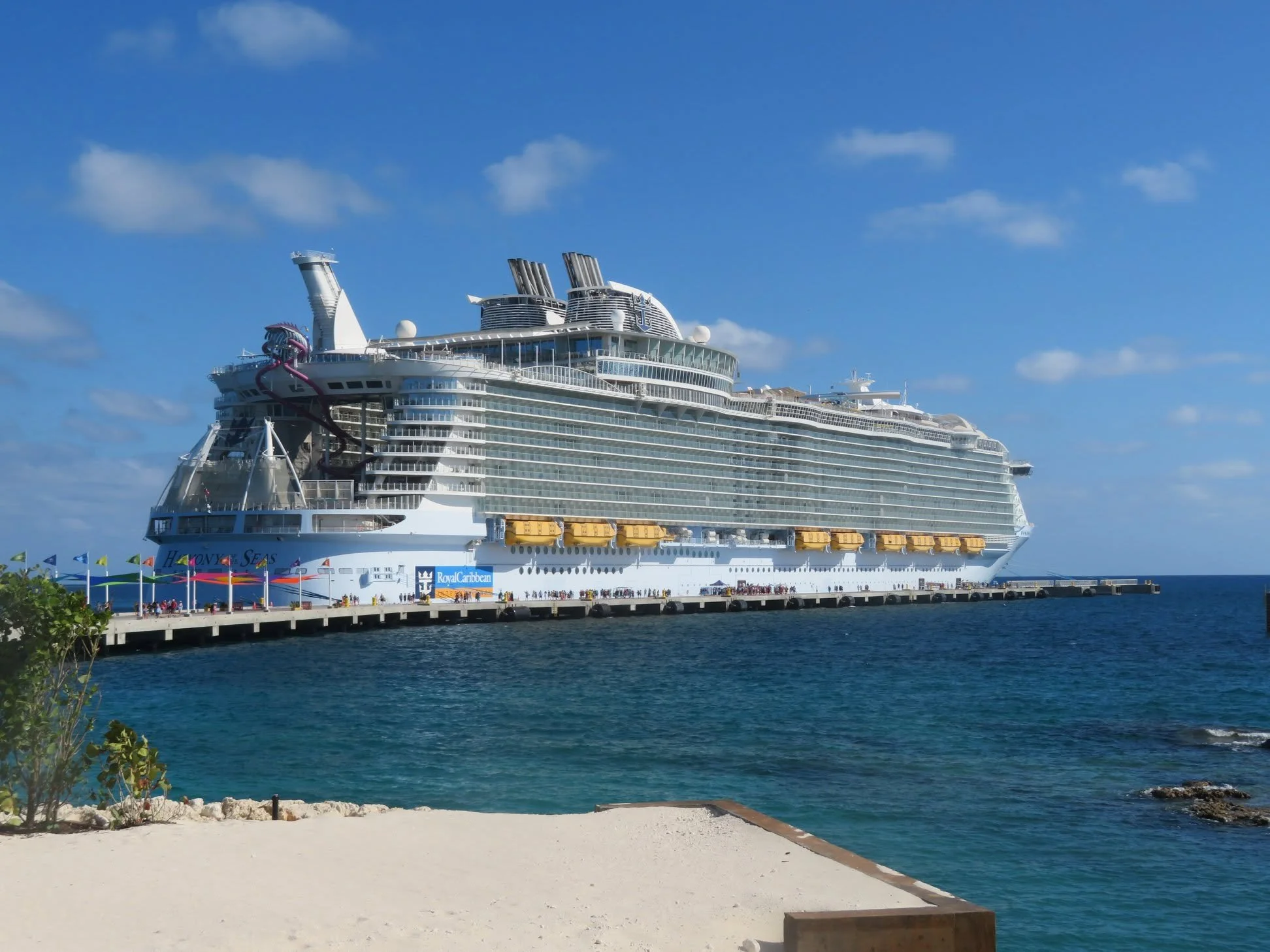 Royal Caribbean cruise ship docked beside a tropical island under a clear blue sky