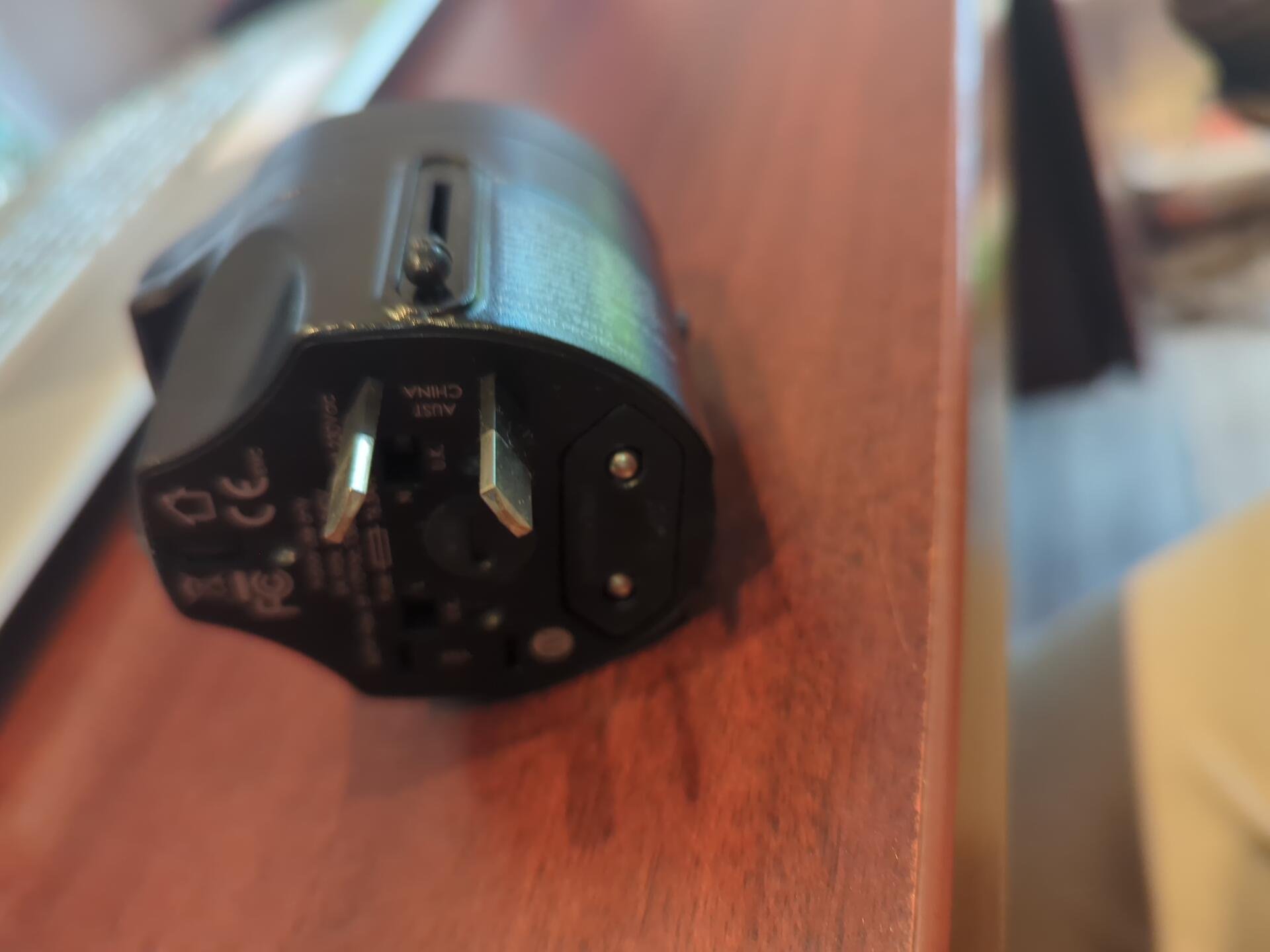 Compact universal travel adapter shown with different international plug configurations, carried as a backup to an international travel power strip.