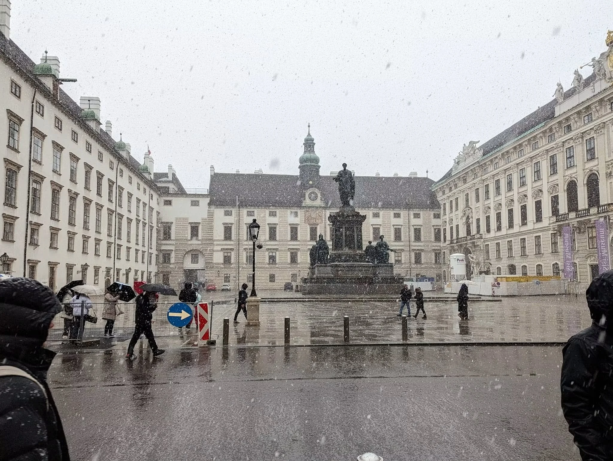 Snow falling over a historic square in Vienna, Austria, as pedestrians cross the wet pavement during a December Viking river cruise excursion.