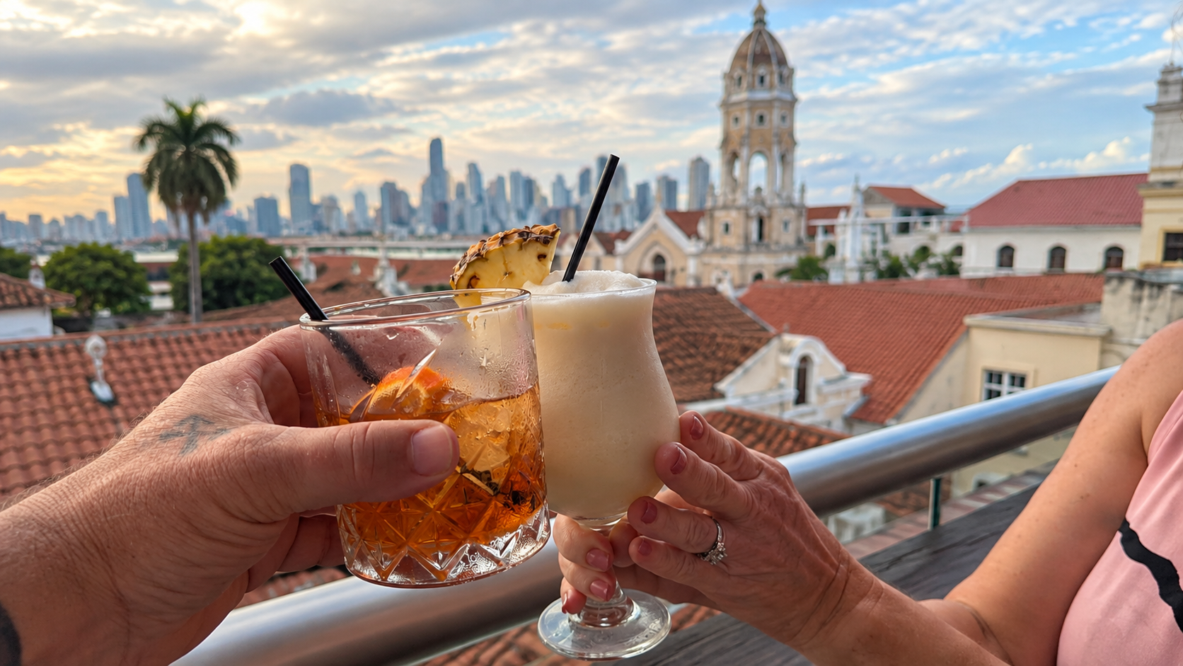 Old Fashioned and frozen rum cocktail raised for a toast from a rooftop overlooking Casco Viejo in Panama City.