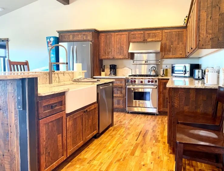 Spacious kitchen in a Powell Butte vacation apartment with rustic wooden cabinets, farmhouse sink, stainless-steel range, and wood flooring.