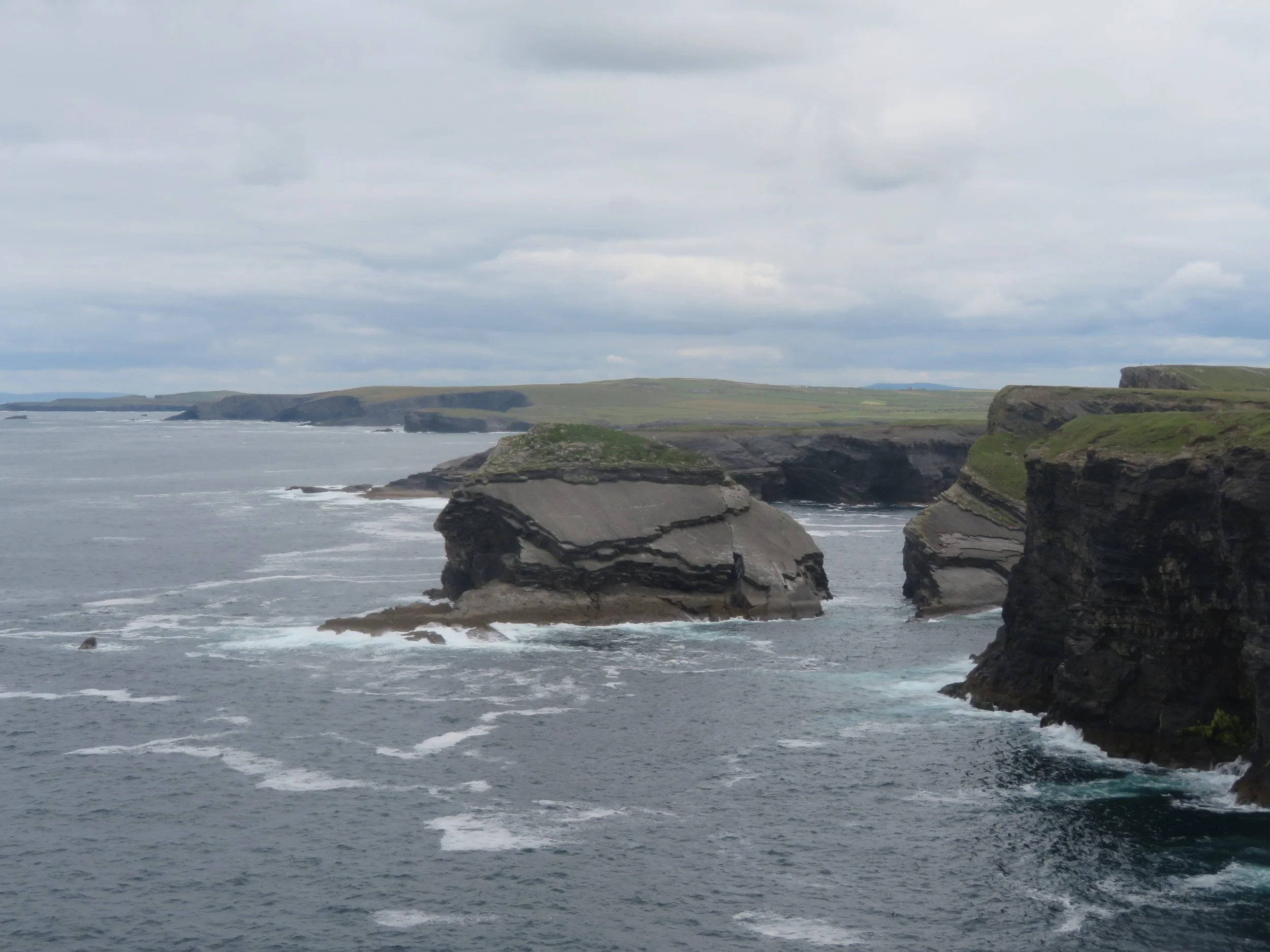 Kilkee Cliffs on Ireland's Atlantic coast, with dramatic layered rock formations, green headlands and waves breaking below.