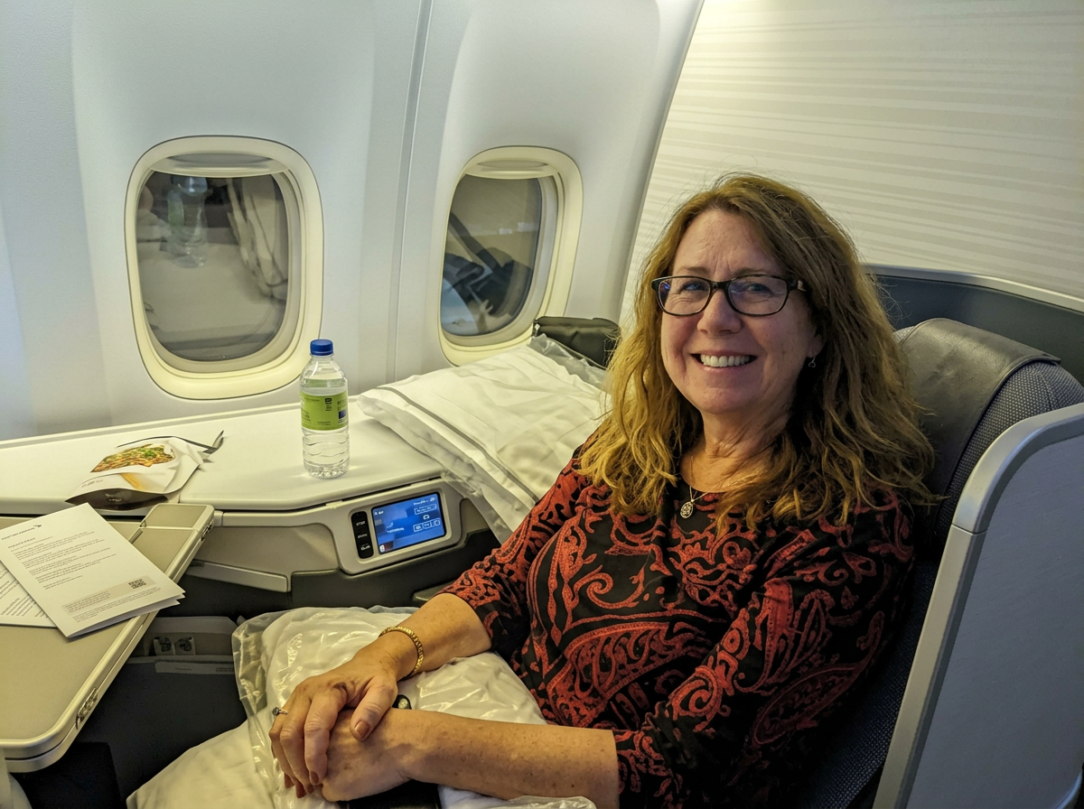 Traveler seated beside the window in a spacious premium-cabin airline seat with bedding and a large tray table