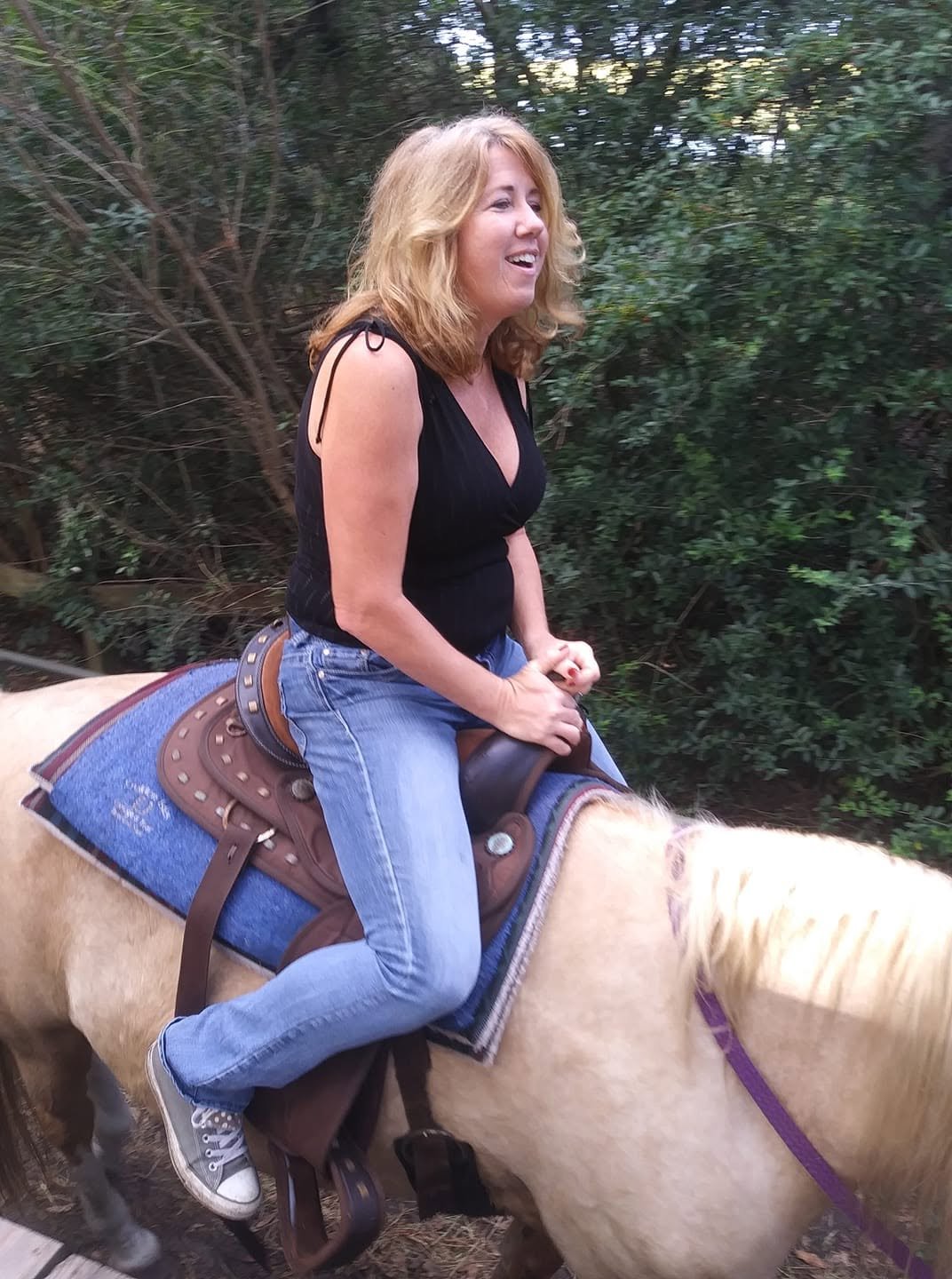 Gina riding a light-colored horse along a wooded trail during a horseback-riding excursion on Jekyll Island.