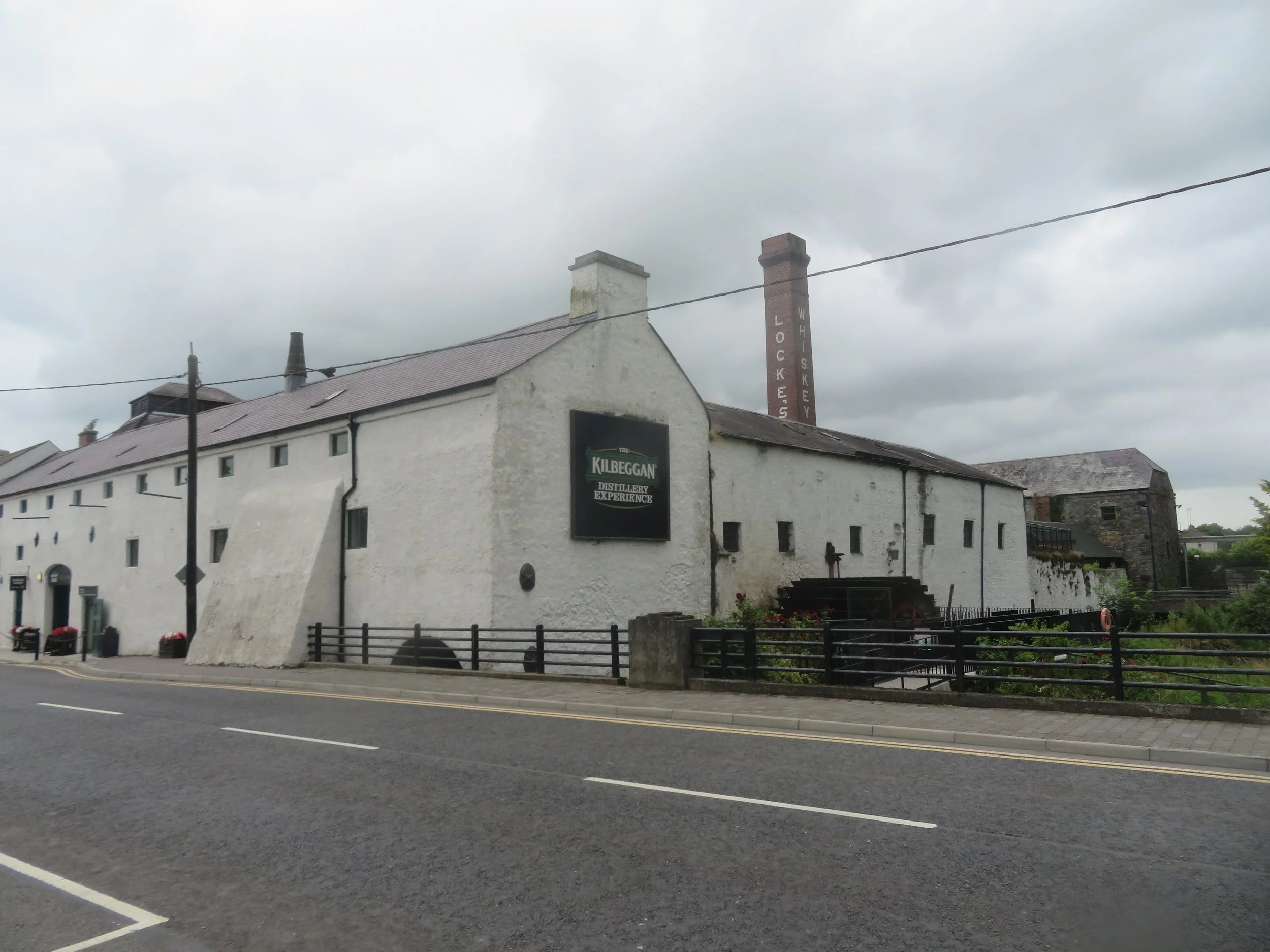Exterior of Kilbeggan Distillery in County Westmeath, Ireland, with its historic whitewashed buildings, Locke’s Whiskey chimney and old waterwheel.