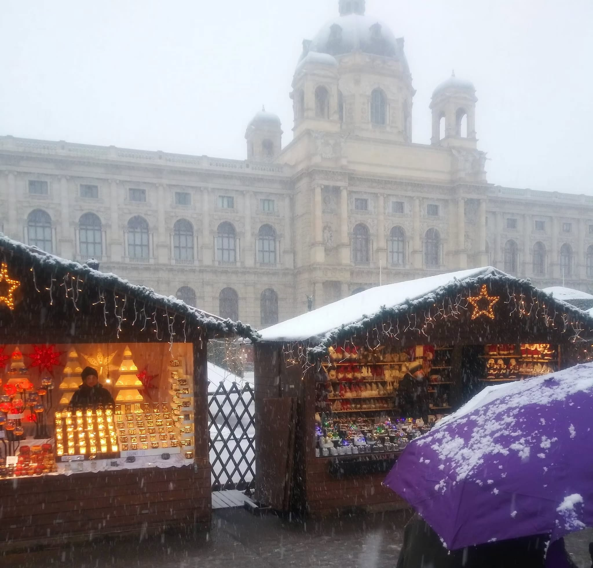 Snow falling over illuminated Christmas market stalls at Vienna's Maria-Theresien-Platz, Austria, during December 2023.