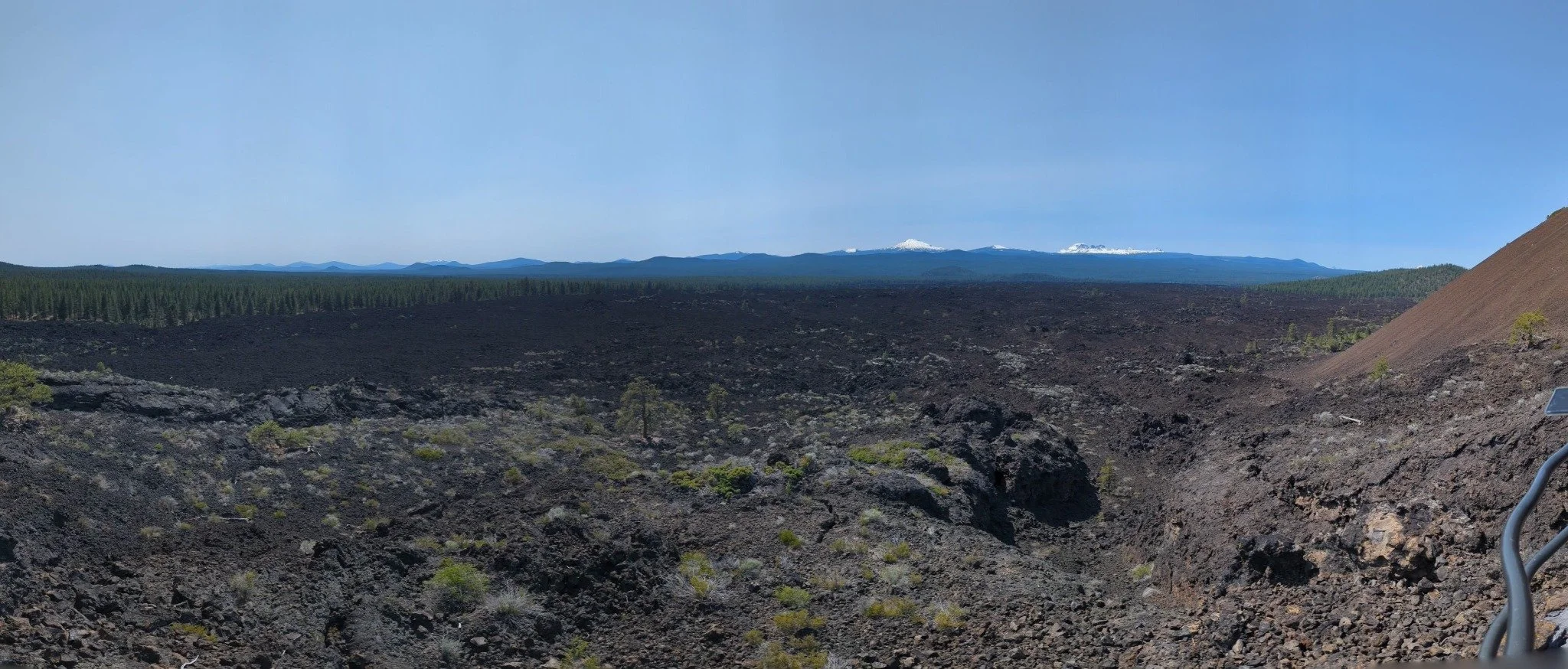 Panoramic view of an expansive black volcanic lava field and distant snowcapped Cascade Mountains from Lava Butte in Central Oregon.