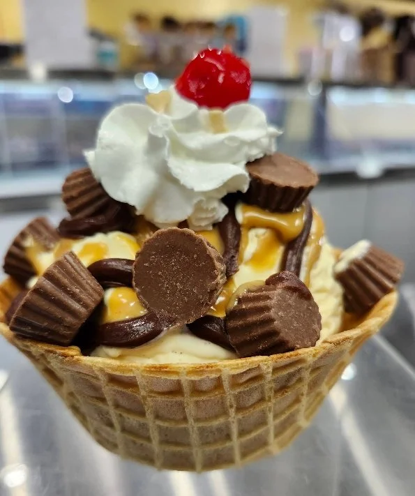 Reese's Peanut Butter Cup ice cream sundae in a waffle bowl, topped with chocolate sauce, peanut butter cups, whipped cream, and a cherry at Sugar Pine Treats in Oregon.