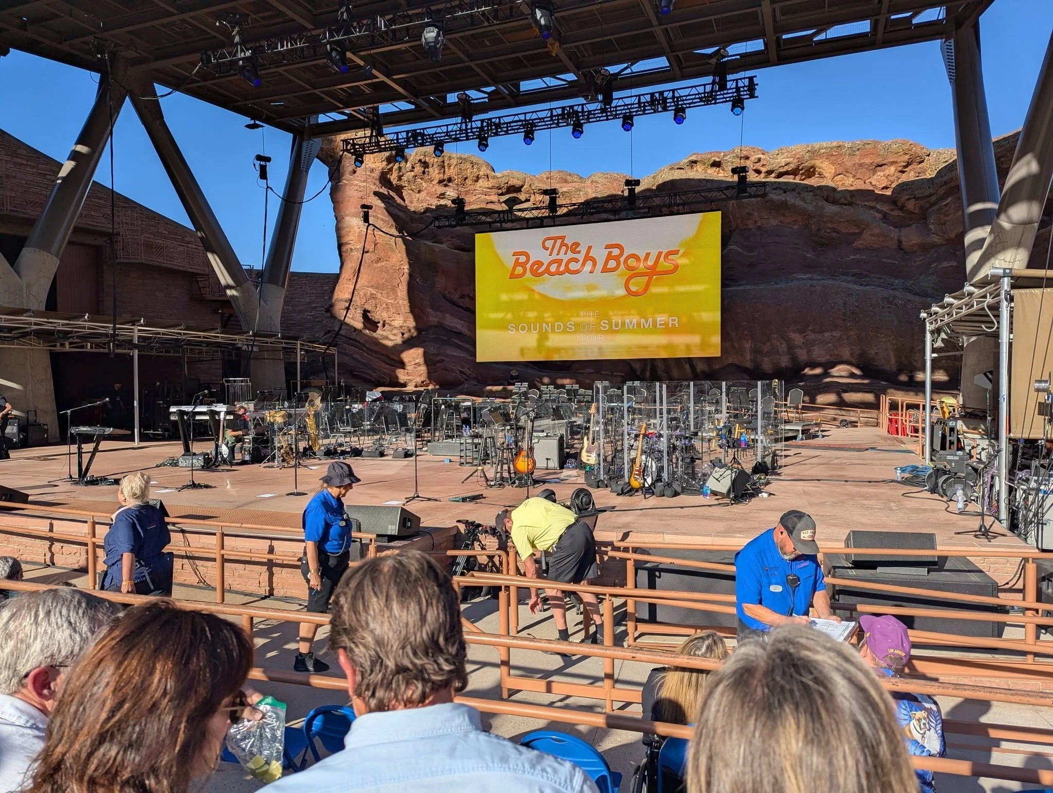 Beach Boys Sounds of Summer stage at Red Rocks Amphitheatre before the concert, with guitars, microphones, orchestra seating, and the tour screen visible.