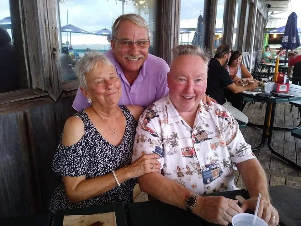 Adult son smiling with his father and stepmother during a family trip together.