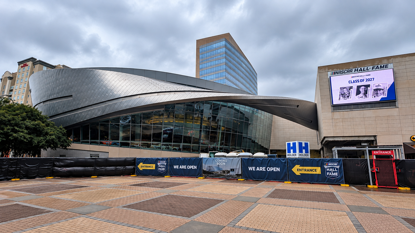 Exterior of the NASCAR Hall of Fame in Charlotte, North Carolina, beneath an overcast sky during a NASCAR race weekend.