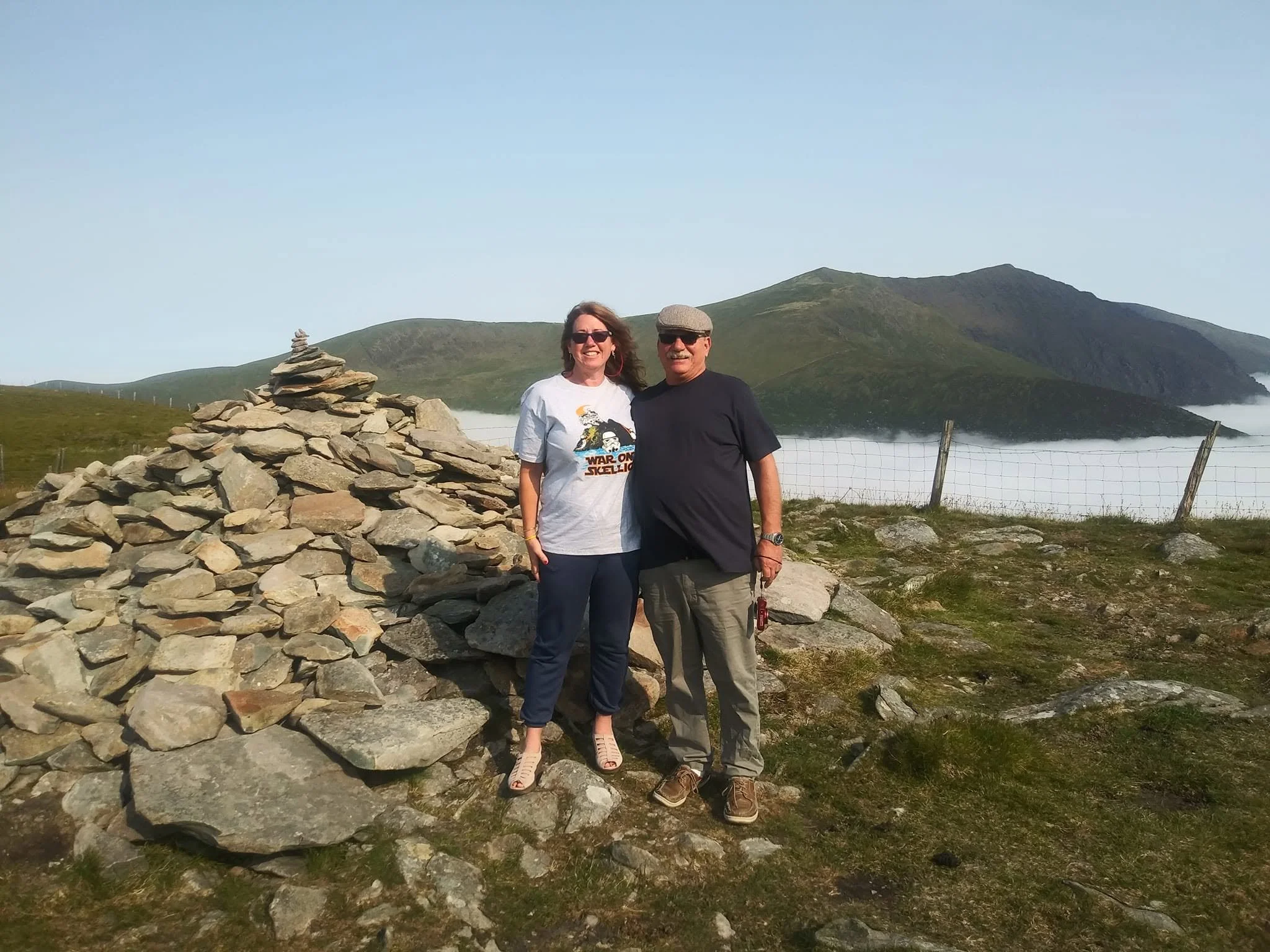 Brian and Gina beside a stone cairn in the Irish countryside during their 2022 road trip.