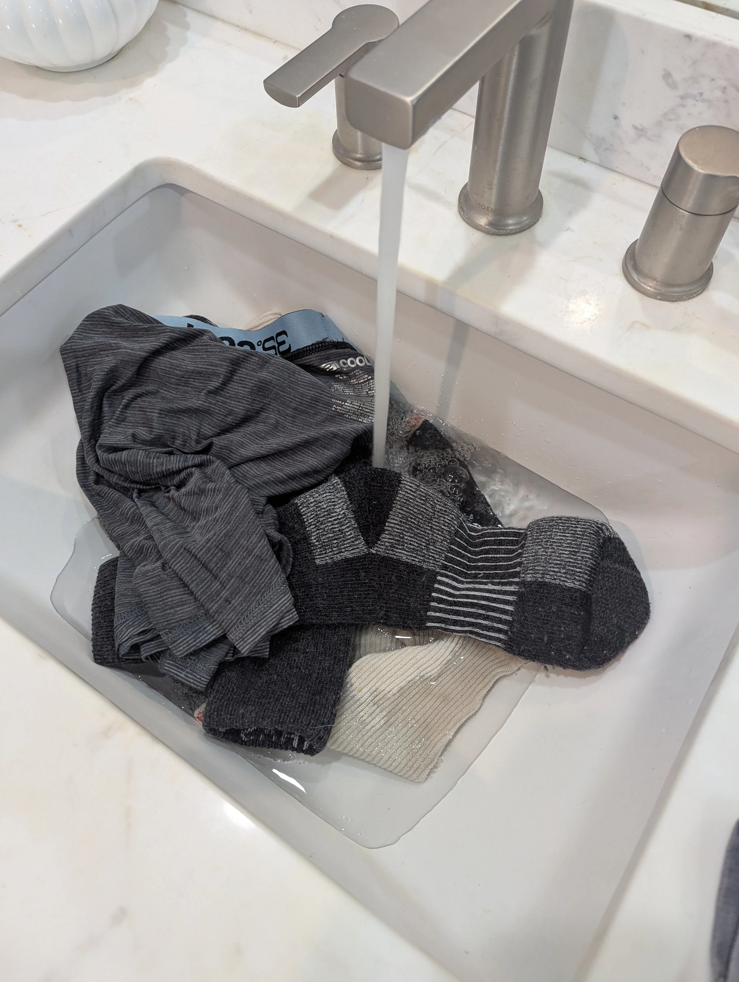 Socks and lightweight travel clothing soaking in a bathroom sink during a travel laundry test.