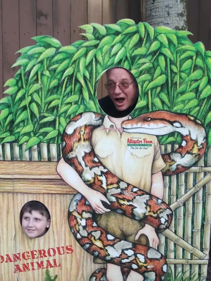 Family posing with their faces through a humorous painted snake photo board at the St. Augustine Alligator Farm in Florida.