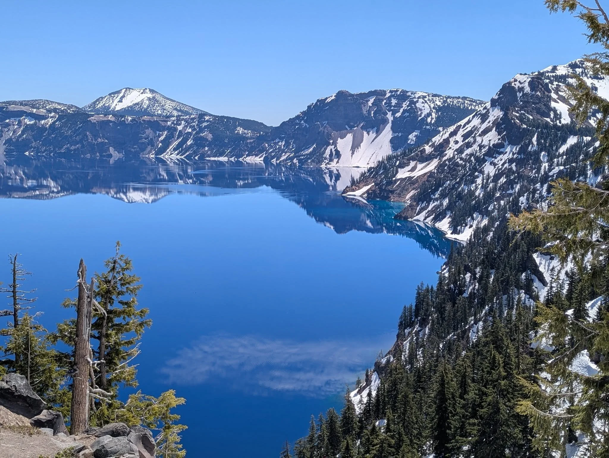 a peaceful crater lake, smooth mirror like water. snow on the mountains. slowly melting in the late spring