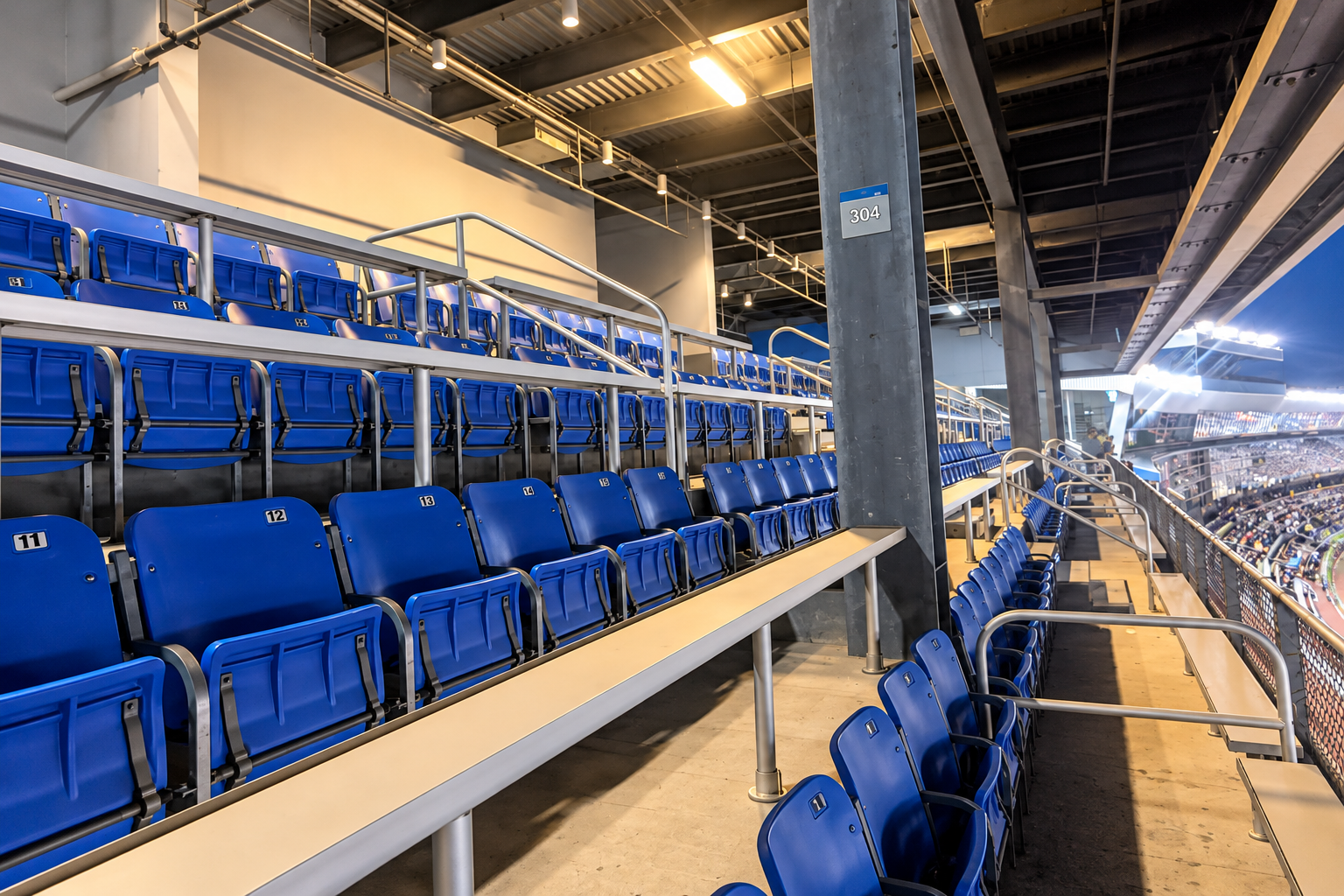 View from covered premium seating at Charlotte Motor Speedway, showing blue seats, individual tables, pit road, and the racing surface.